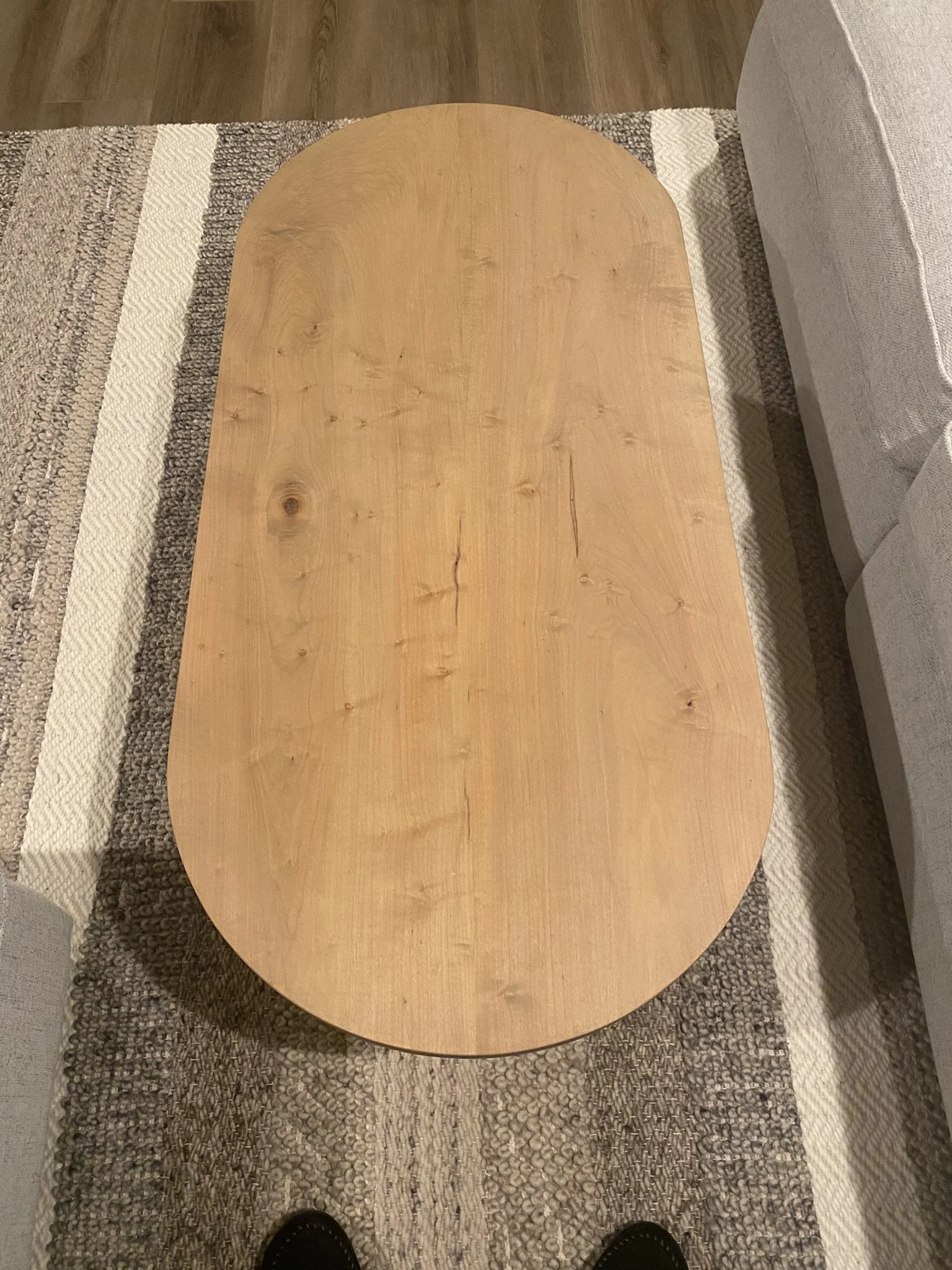 Overhead view of an oval wooden coffee table on a area rug, next to a beige sofa.