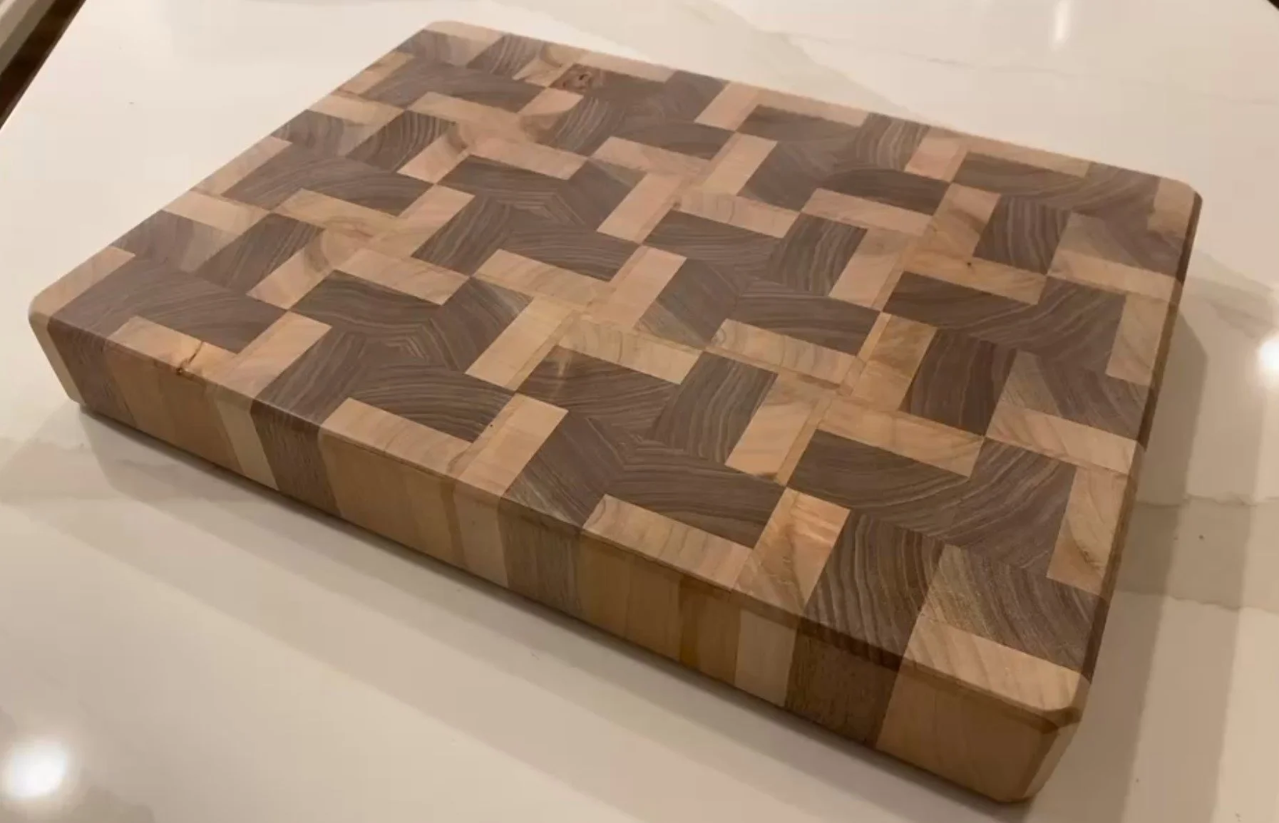 Wooden cutting board with intricate geometric pattern of alternating light and dark wood pieces.
