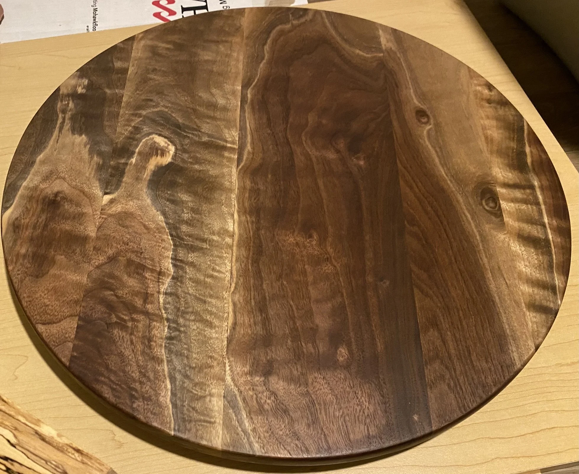 A round wooden cutting board with intricate grain patterns, placed on a light-colored wooden surface.
