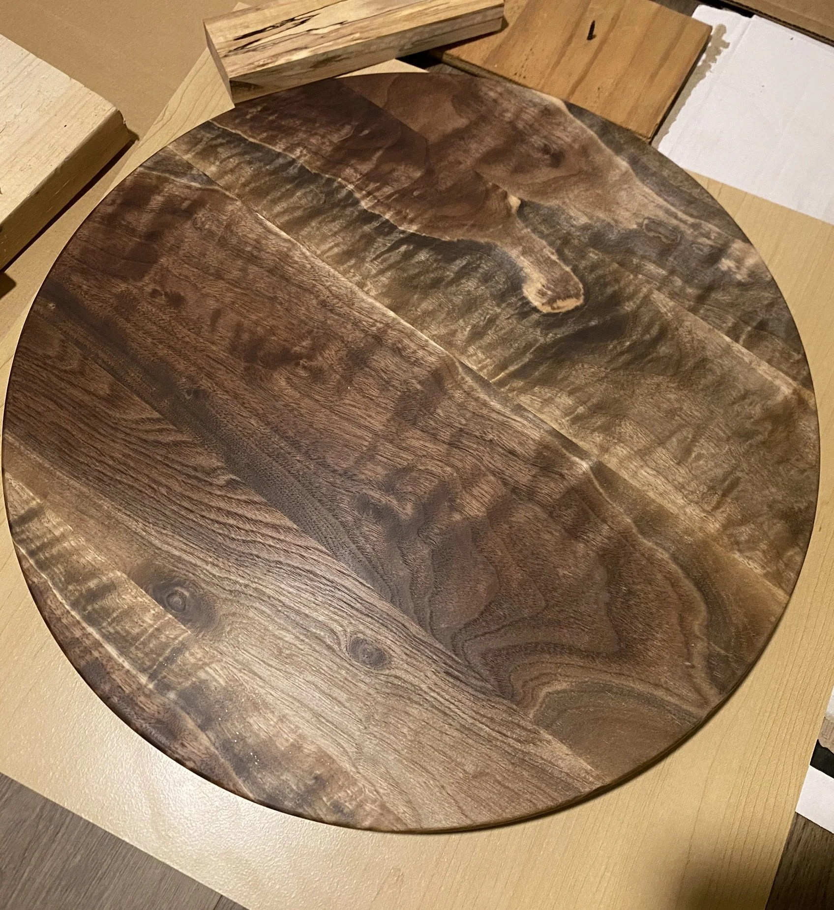 Round wooden table with a dark, natural wood grain finish surrounded by various wood samples or planks.
