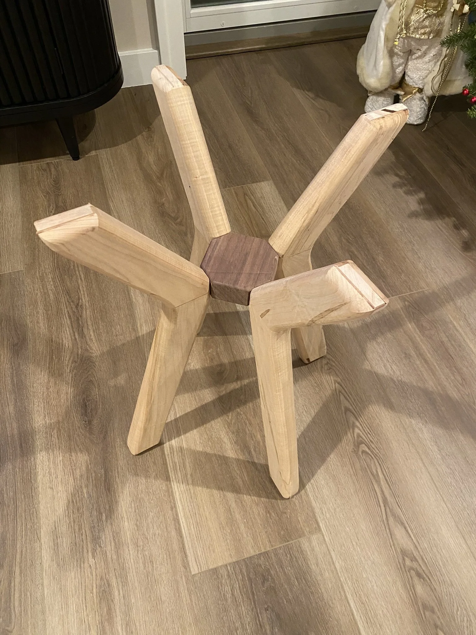 Unassembled wooden chair with five legs and a hexagonal base sitting on a wooden floor.