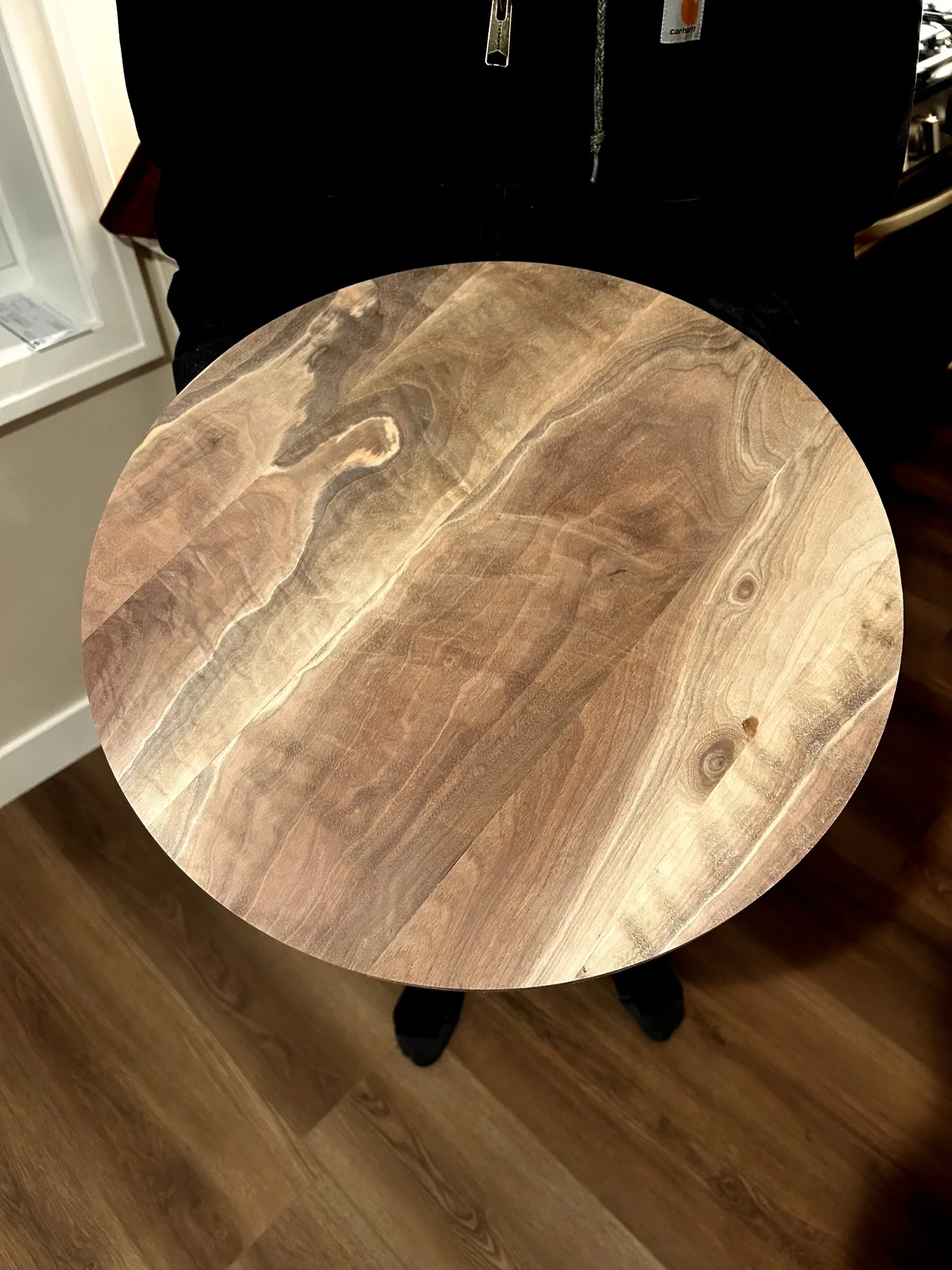 Round wooden table with a natural wood grain pattern, held by a person wearing black clothing.