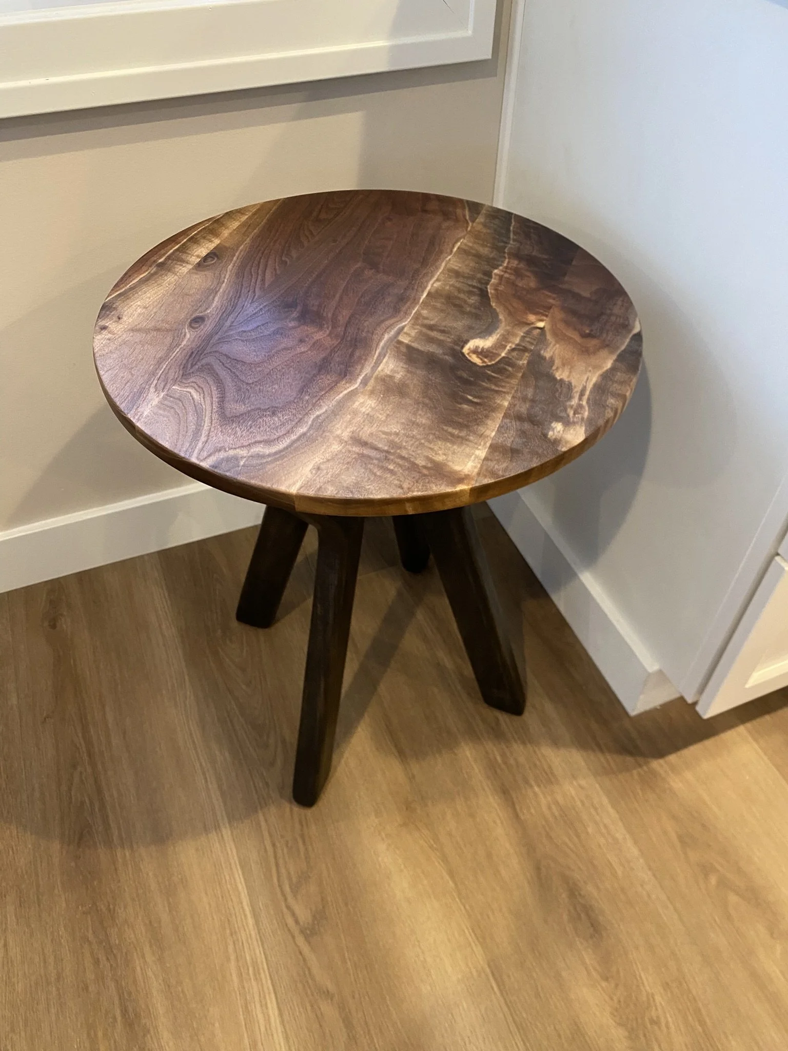 A round wooden side table with a dark wood finish, positioned against a wall and corner of a room.