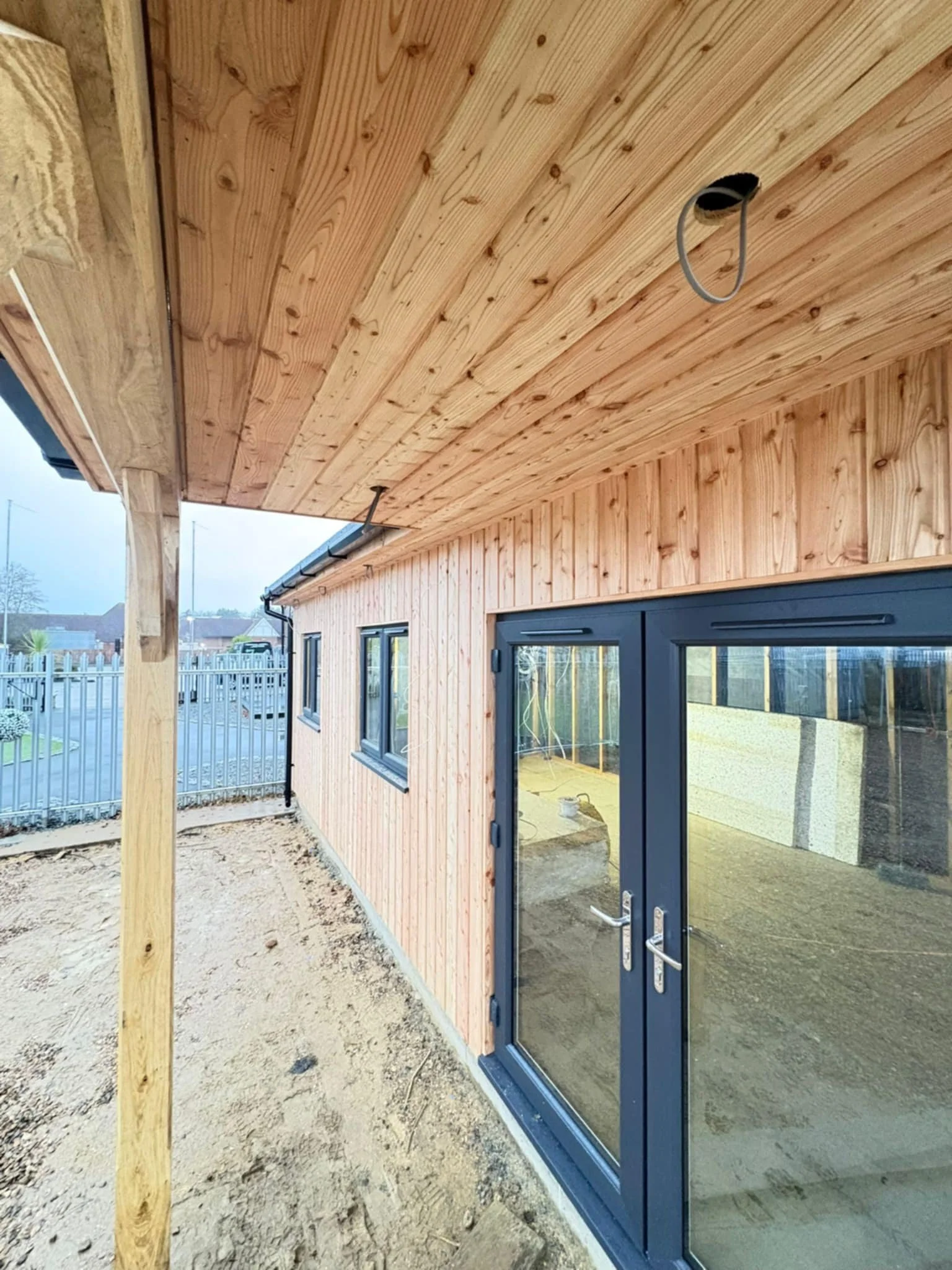 Exterior of a house under construction with wooden siding, a large sliding glass door, and an unfinished porch ceiling.