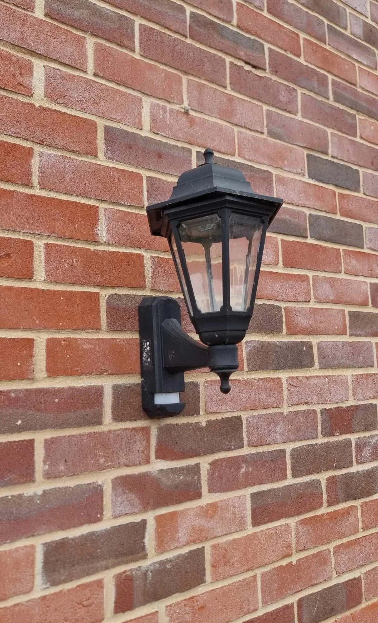 Outdoor black wall-mounted lantern on red brick wall.