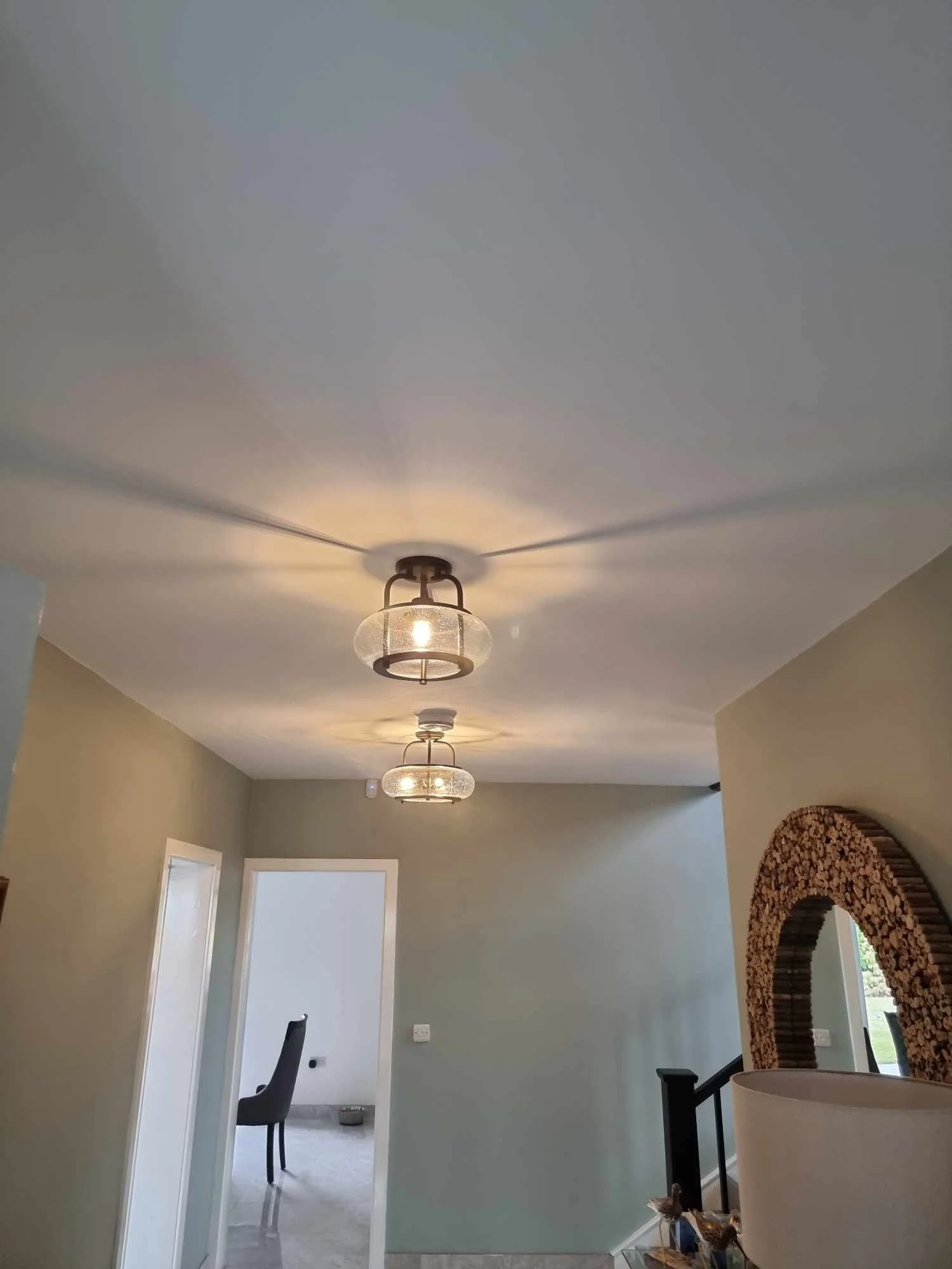 Interior view of a modern home with ceiling lights, open doorways, stairs, and a mirror decorated with logs.