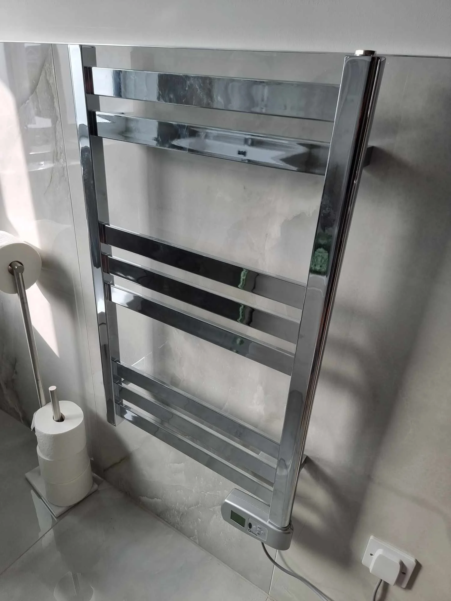 Silver heated towel rail with digital thermostat in a bathroom.