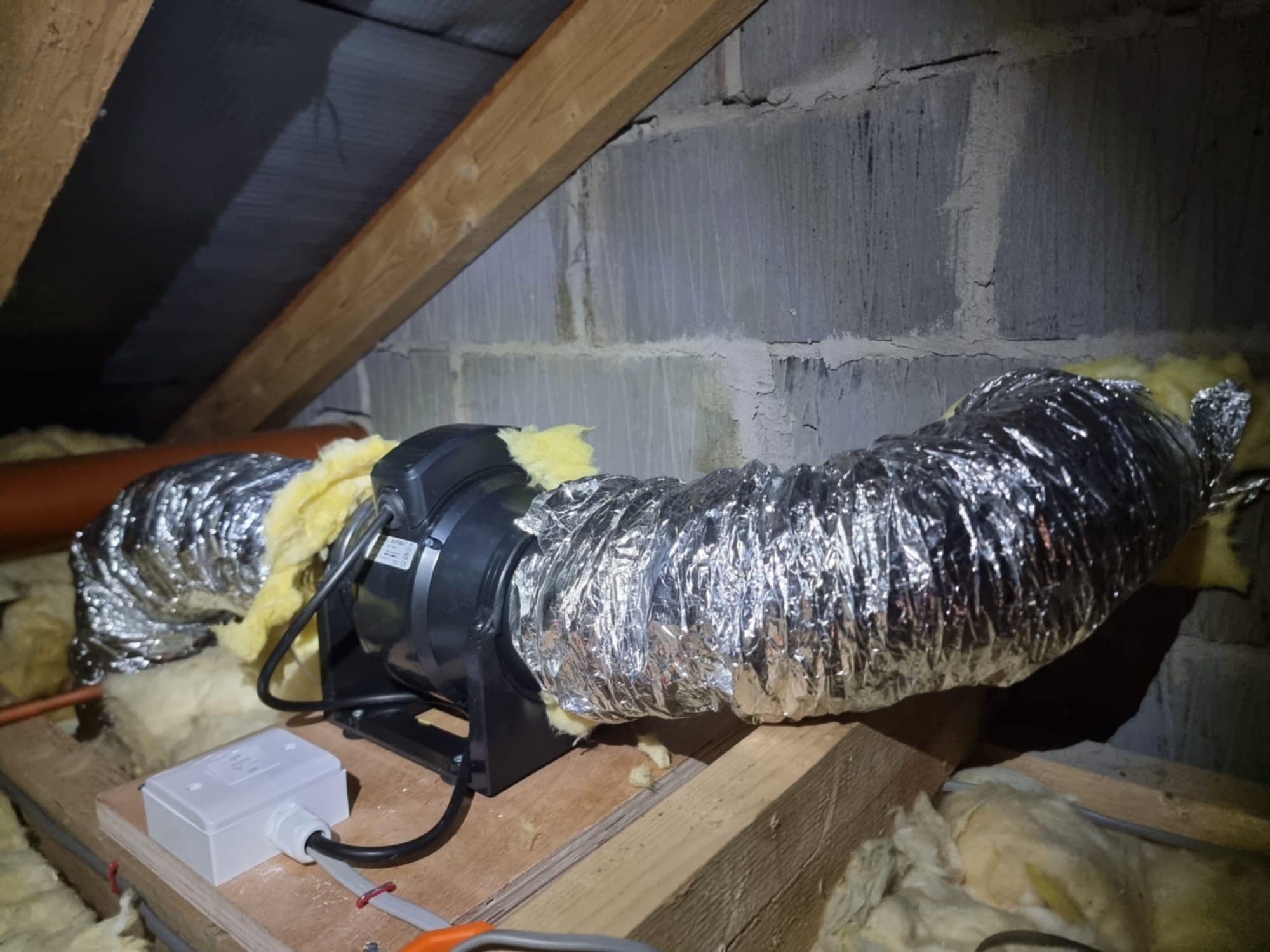 Insulation ductwork installation in an attic space, with exposed duct wrapped in reflective foil insulation, insulation foam, and electrical wiring.
