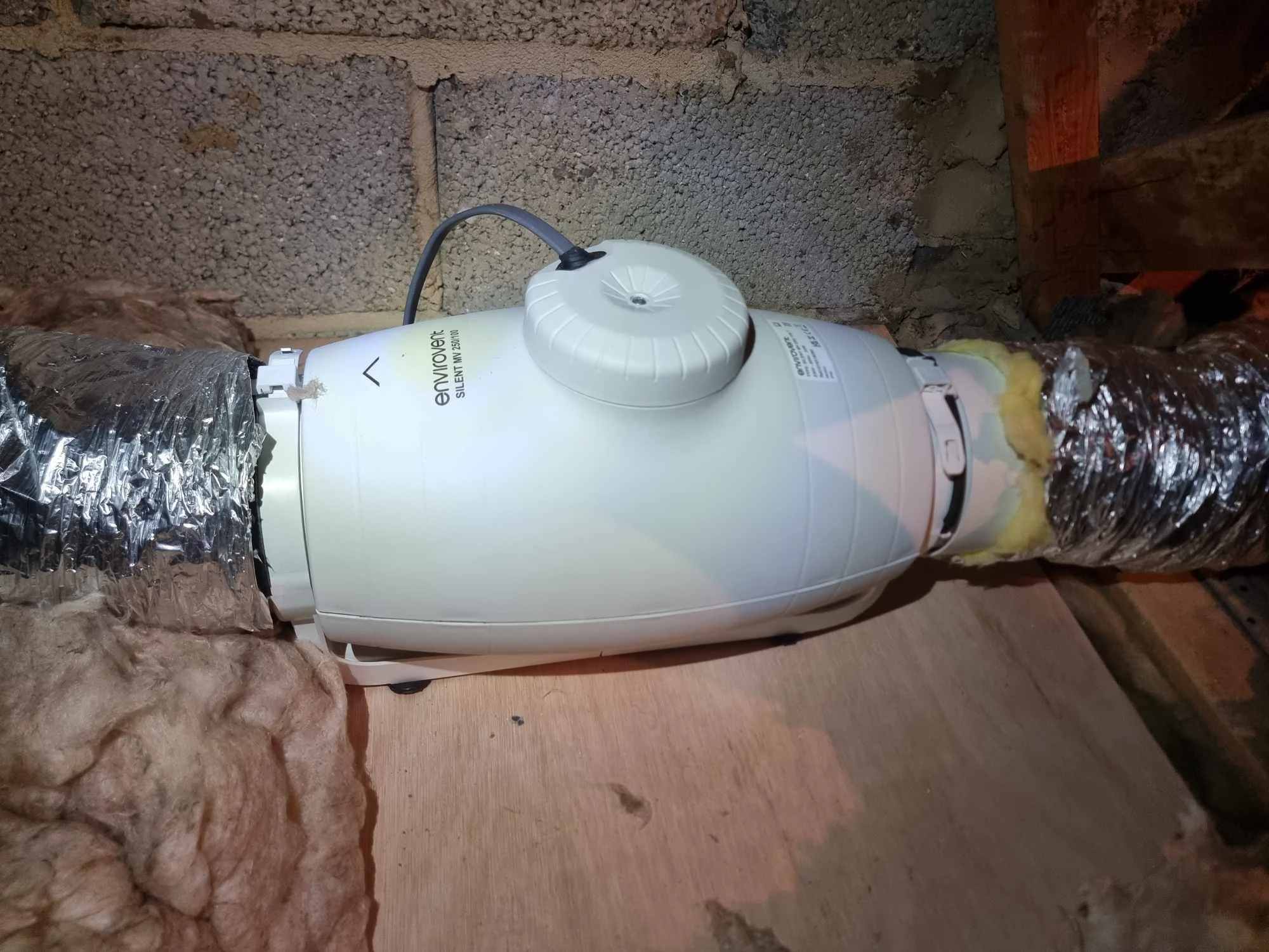 A white basement ventilation fan installed in a wall with exposed insulation and ducting.