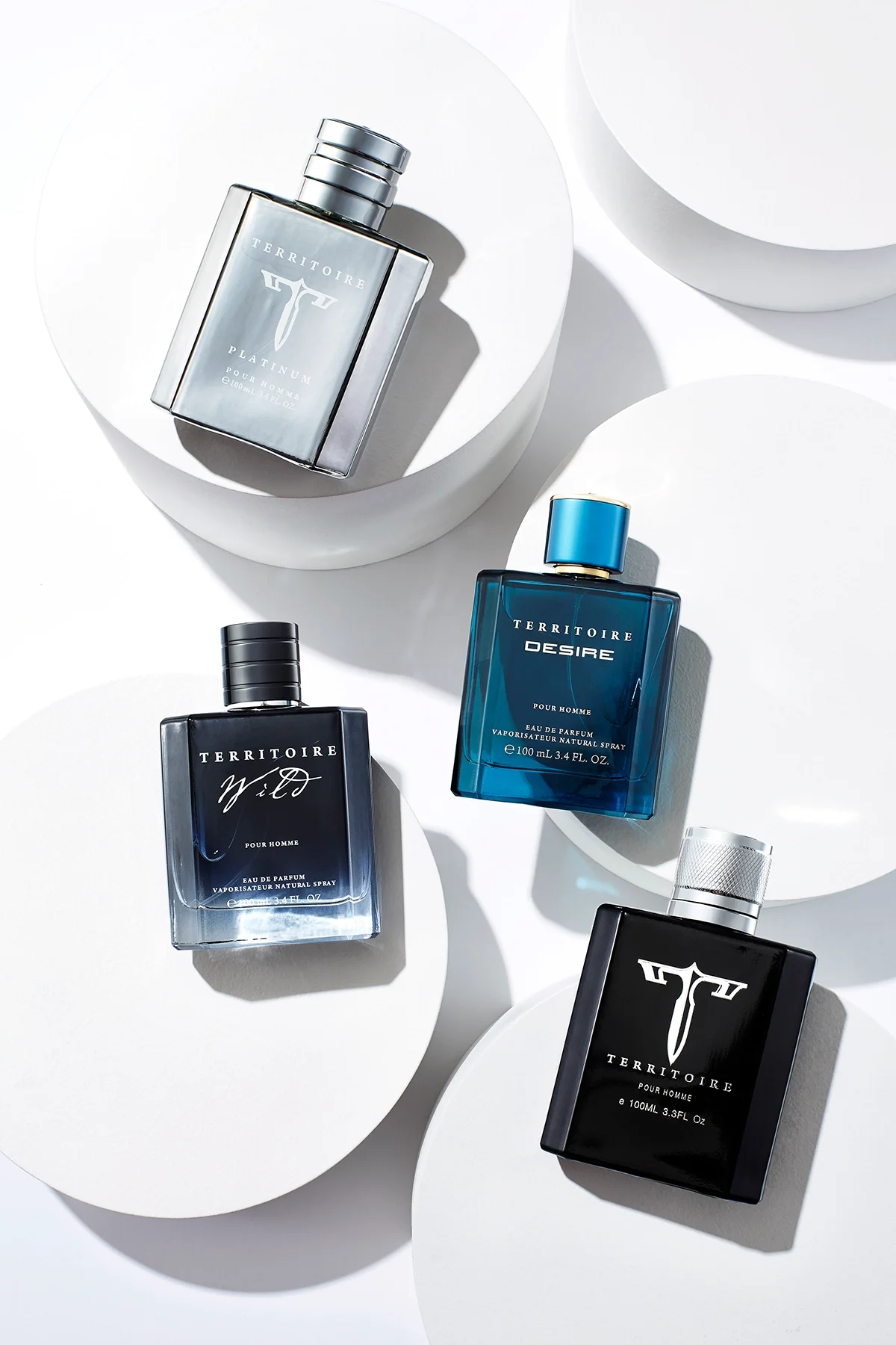 Four bottles of Territoire perfume arranged on white circular stands, with shadows cast on a white background.