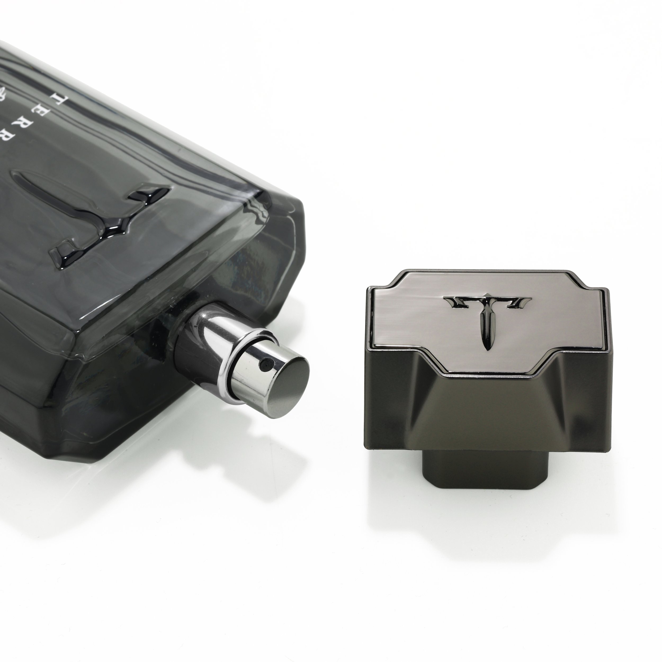 A black perfume bottle with a silver spray nozzle and a matching rectangular cap, both featuring a stylized 'T' emblem on top.