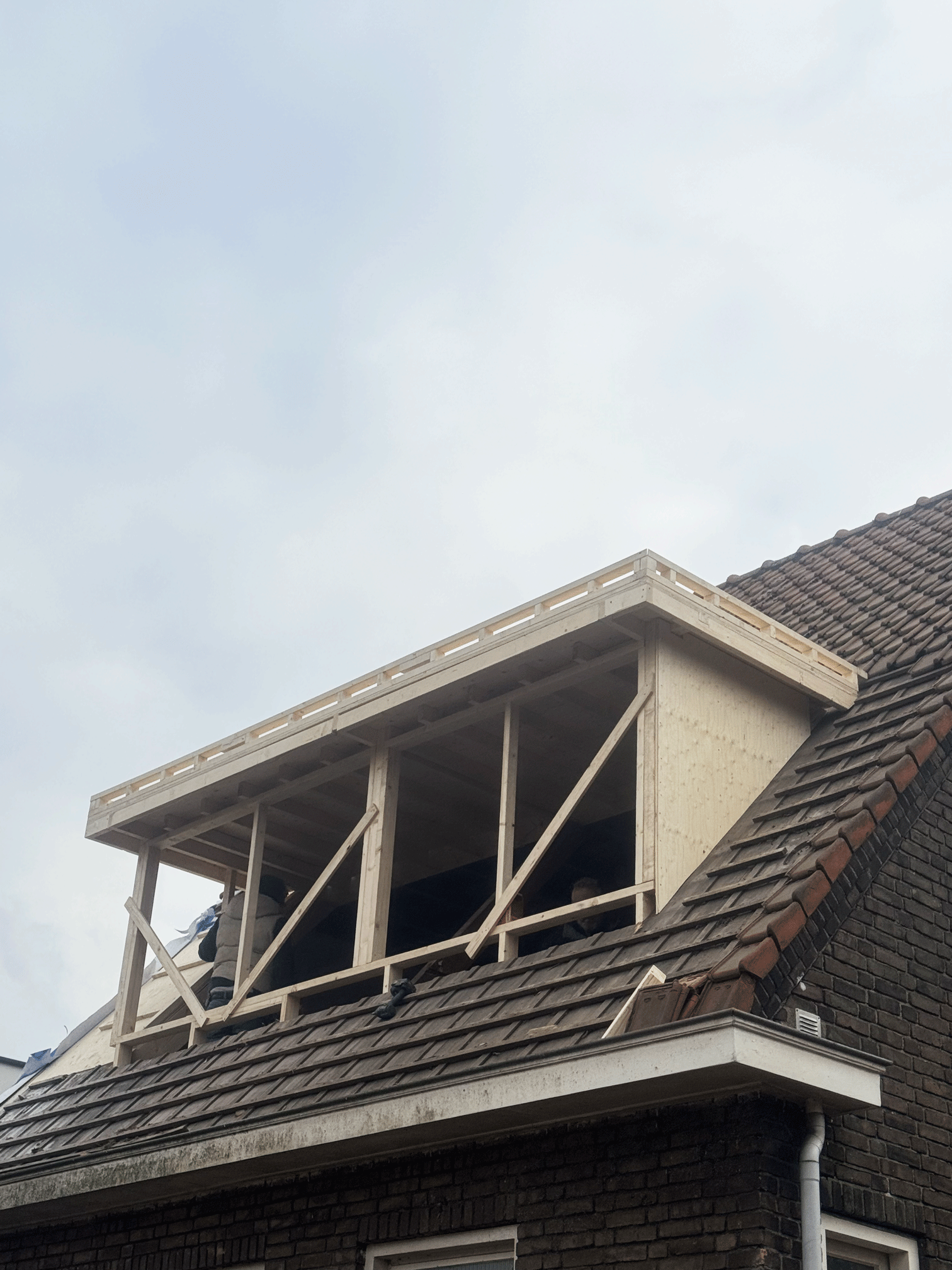 Een huis met een gedeeltelijk nieuwe houten dakkapel onder constructie, met twee mensen die er werken.