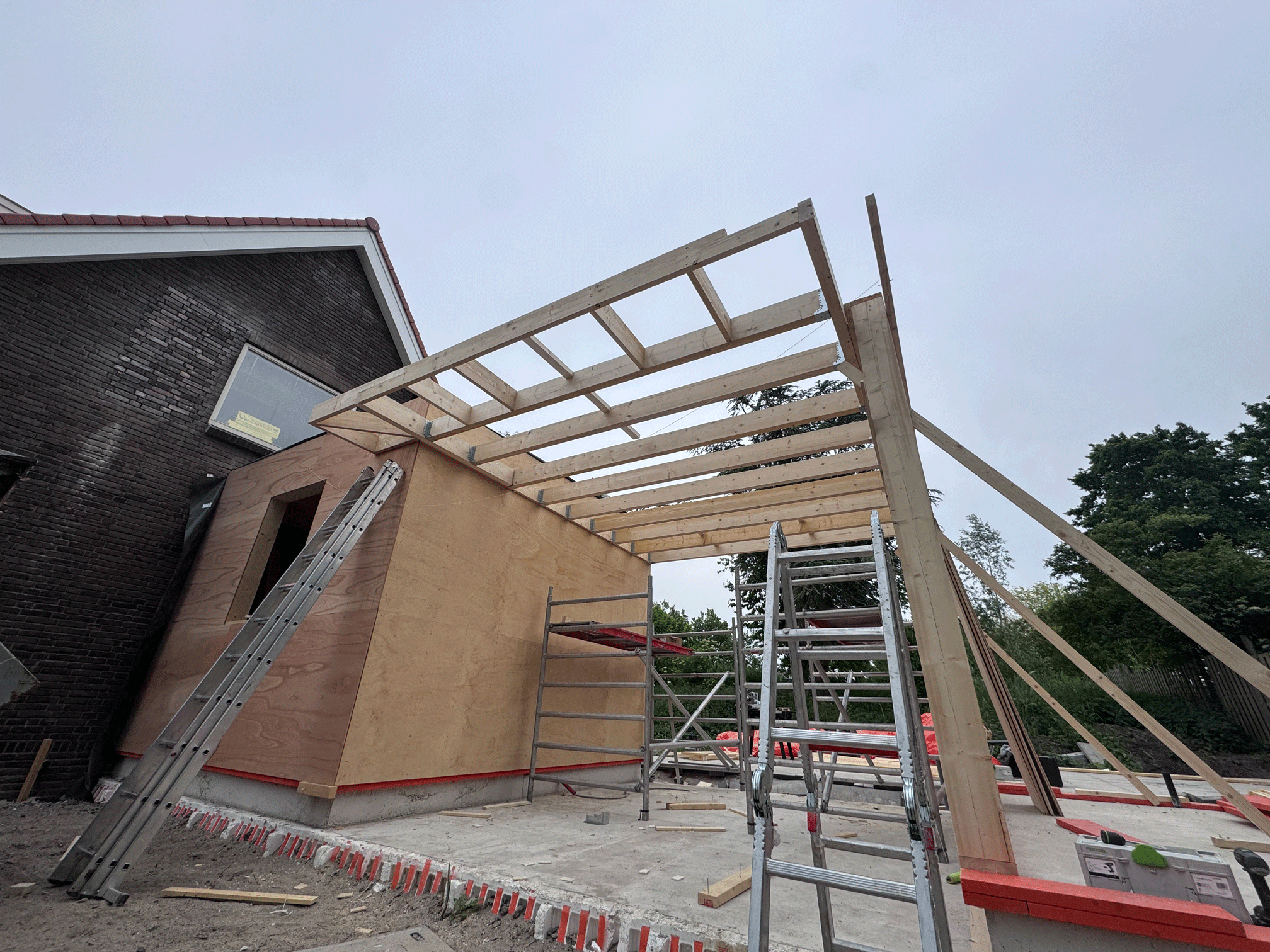 Bouw van een houten structuur van een nieuw gebouw, met ladders en bouwmaterialen op de bouwplaats.
