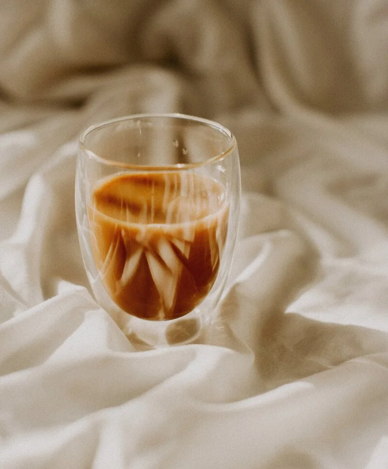 A glass of iced coffee with milk on a crumpled white fabric background.