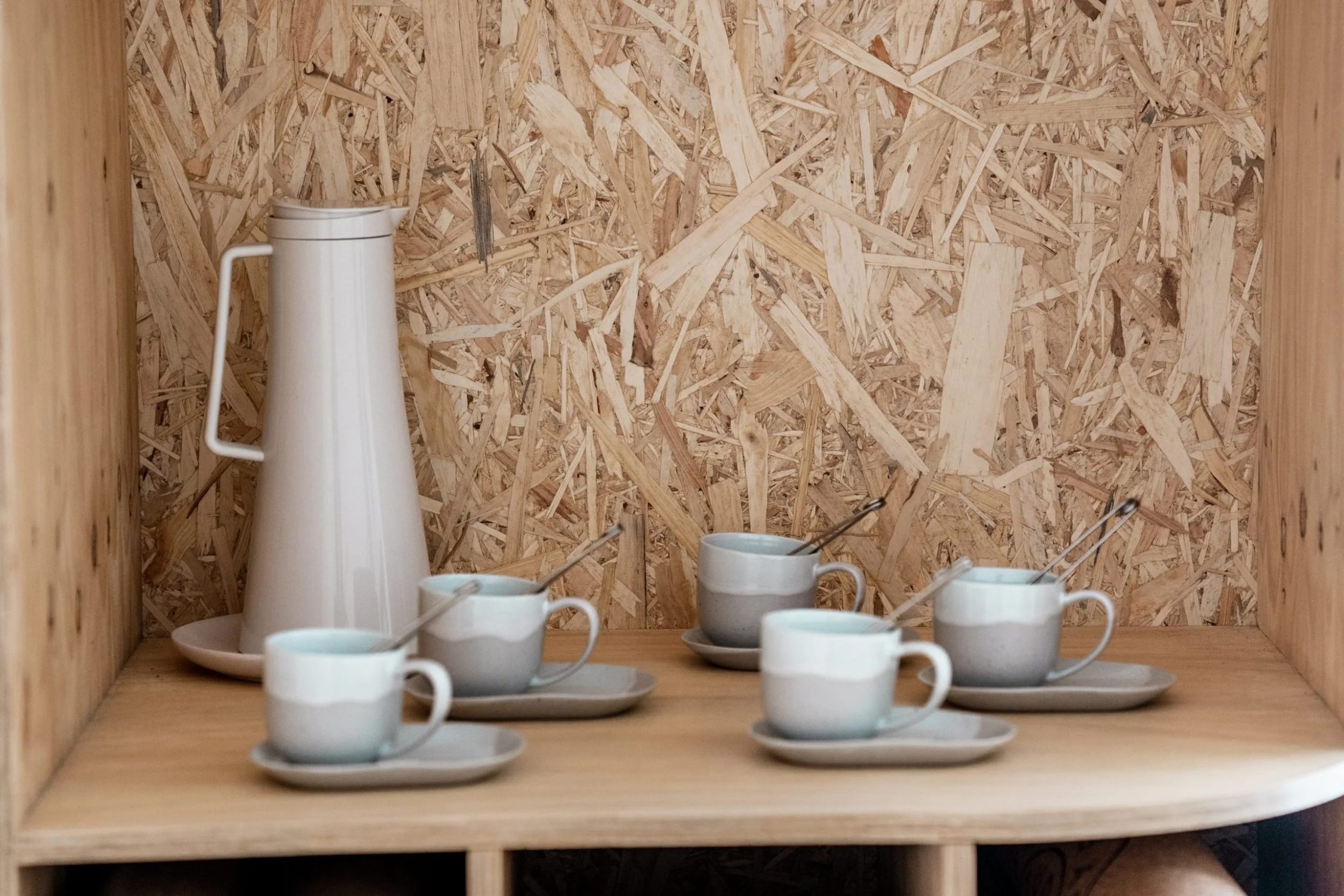 A wooden shelf with a white coffee pot and several matching ceramic cups and saucers arranged on it.