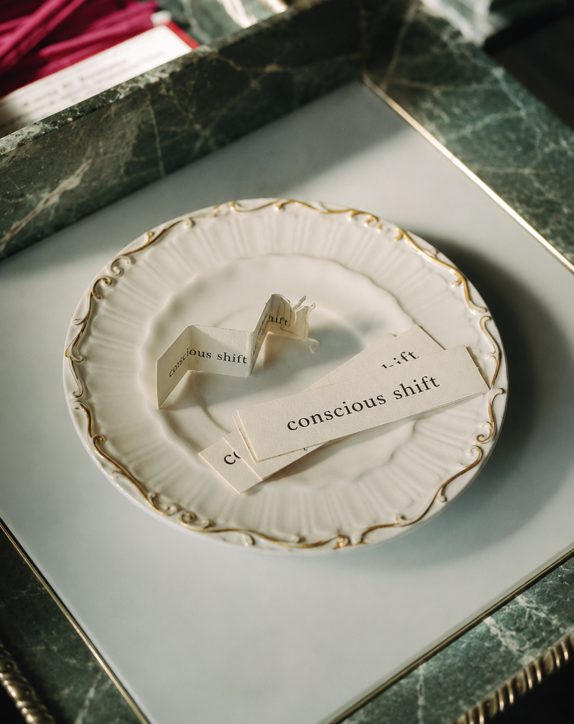 A decorative white ceramic plate with gold trim, holding strips of paper with the words "conscious shift" on them, some standing upright and some lying flat.