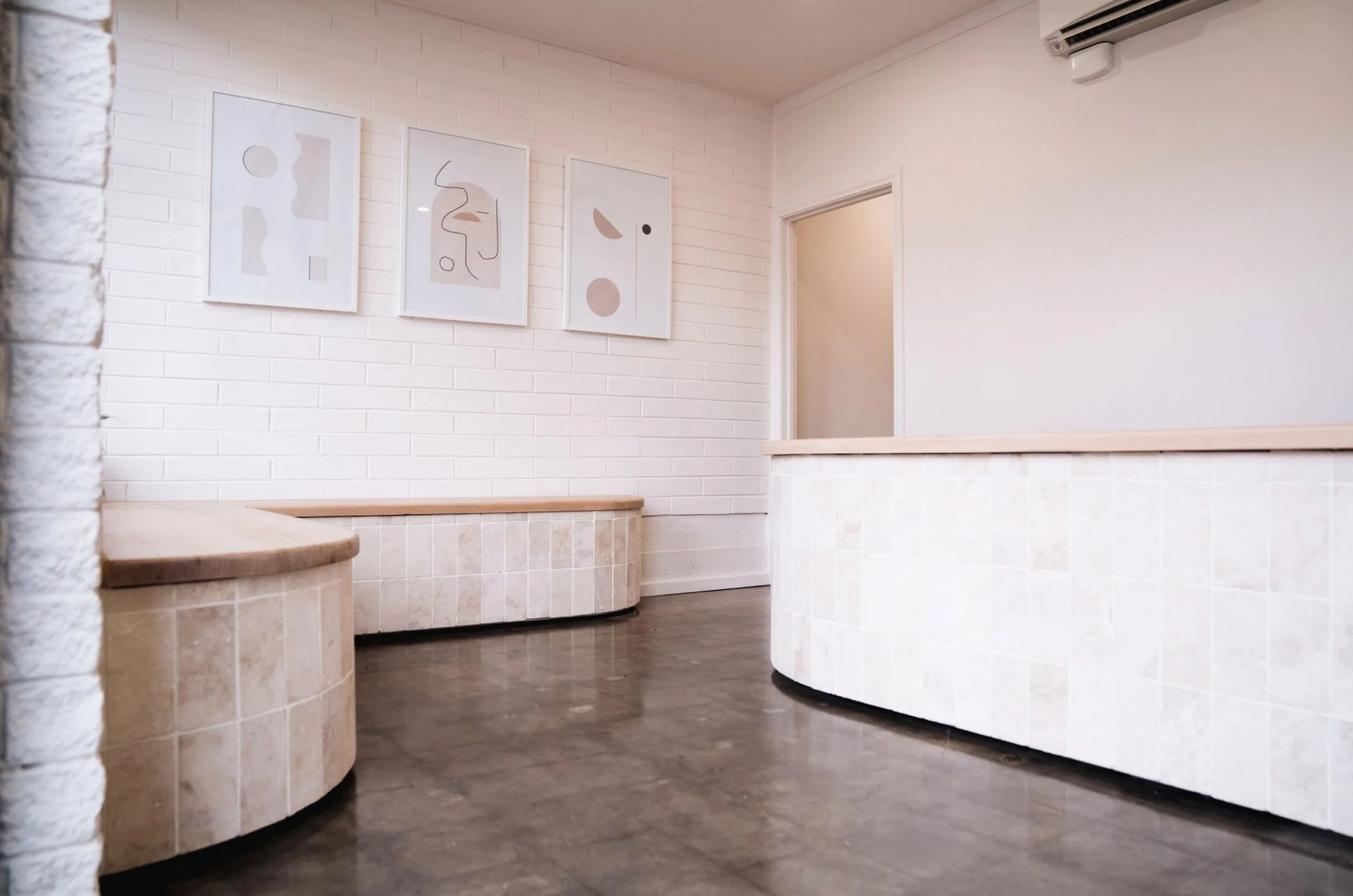 Empty interior space with white brick walls, modern abstract art on the wall, stone benches, and air conditioning unit on the ceiling.