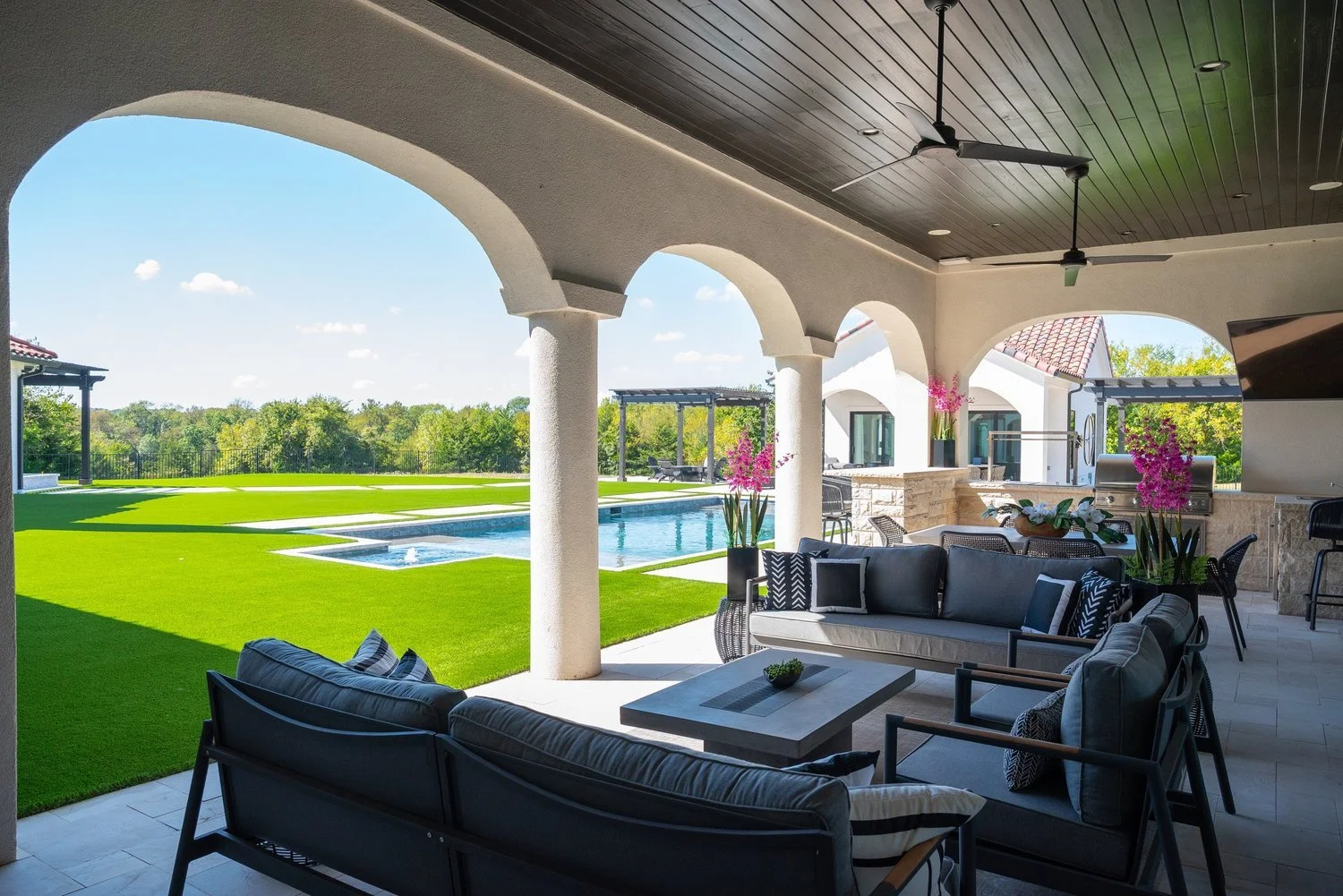 Patio with outdoor lounge area, overlooking a backyard with a swimming pool, green lawn, and trees in the distance