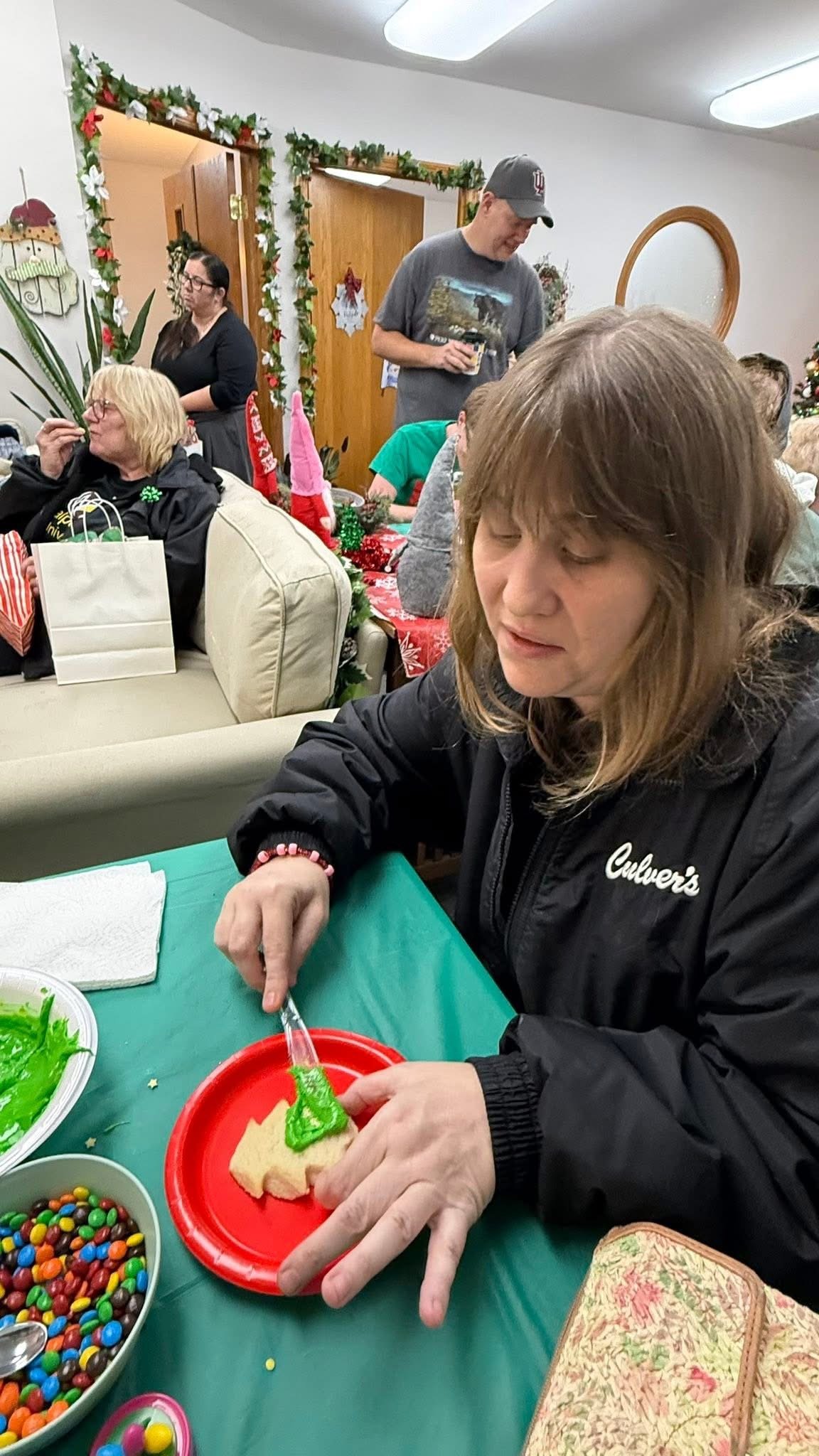 A woman is decorating a sugar cookie with green icing at a holiday gathering.