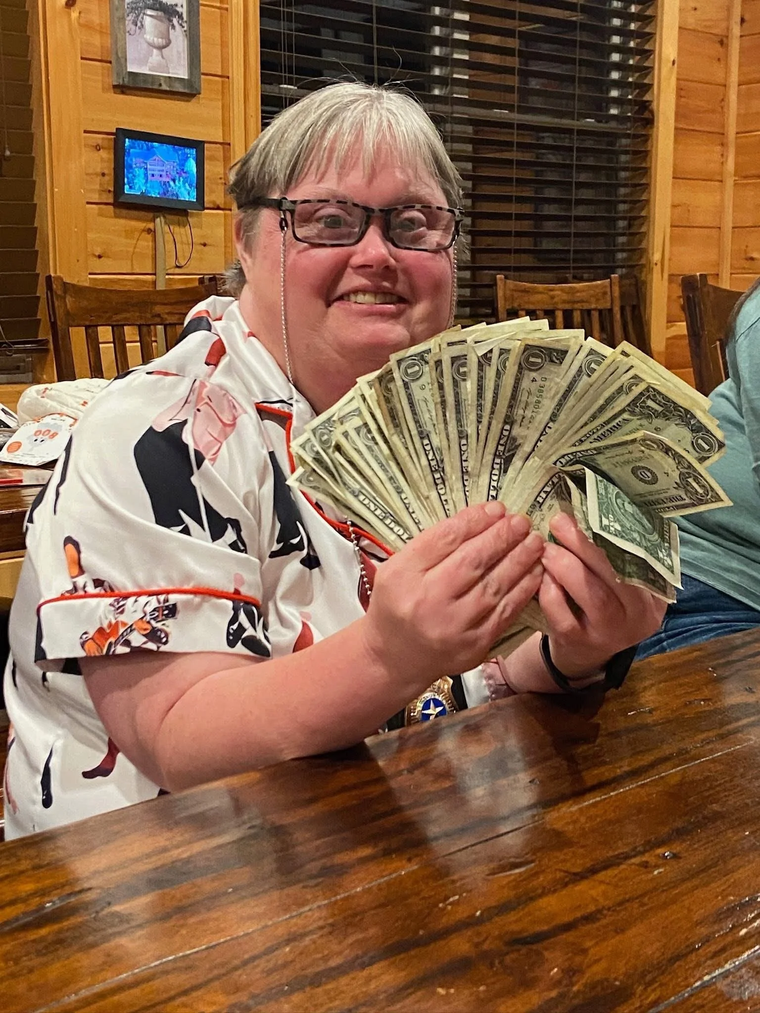 A smiling woman with glasses holding a fan of US dollar bills.