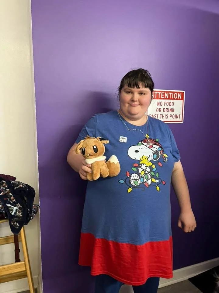 A girl holds a plush Toy Story character, Slinky Dog, in a room with a purple wall and a sign that reads 'Attention: No Food or Drink Past This Point'.