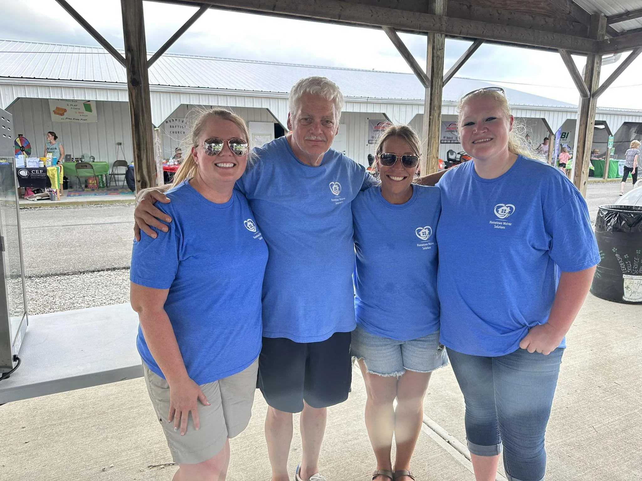Four people in blue shirts standing under a pavilion, smiling for a photo.