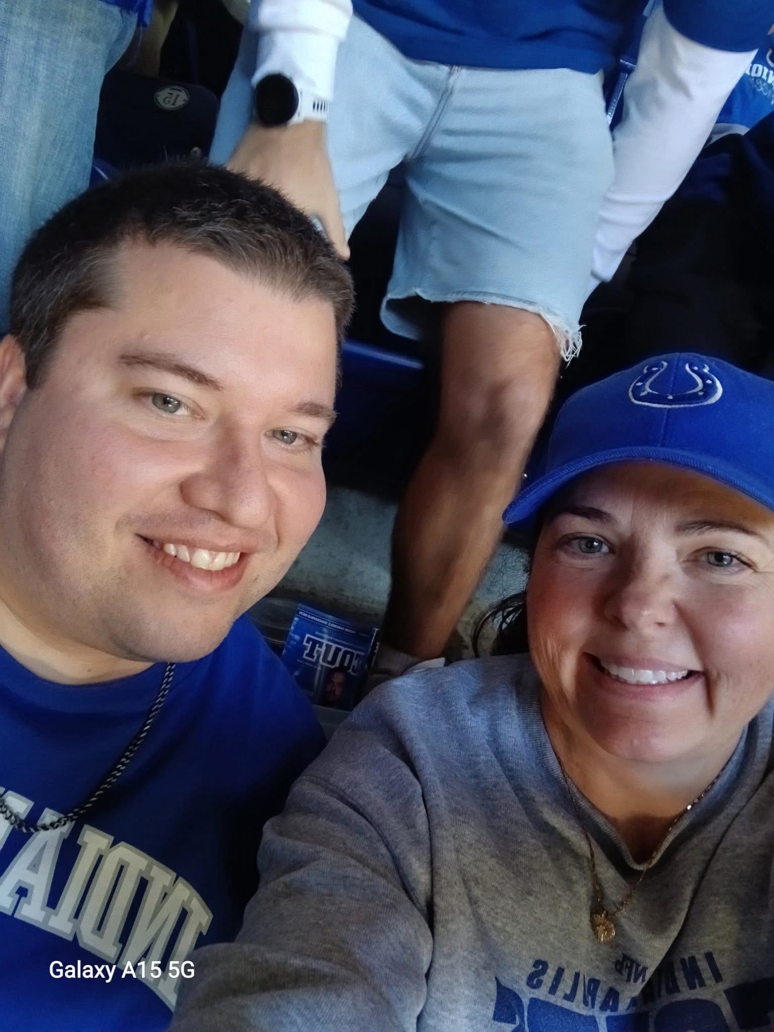Two smiling fans at a sports event, a man and a woman, with a man in the background wearing shorts.