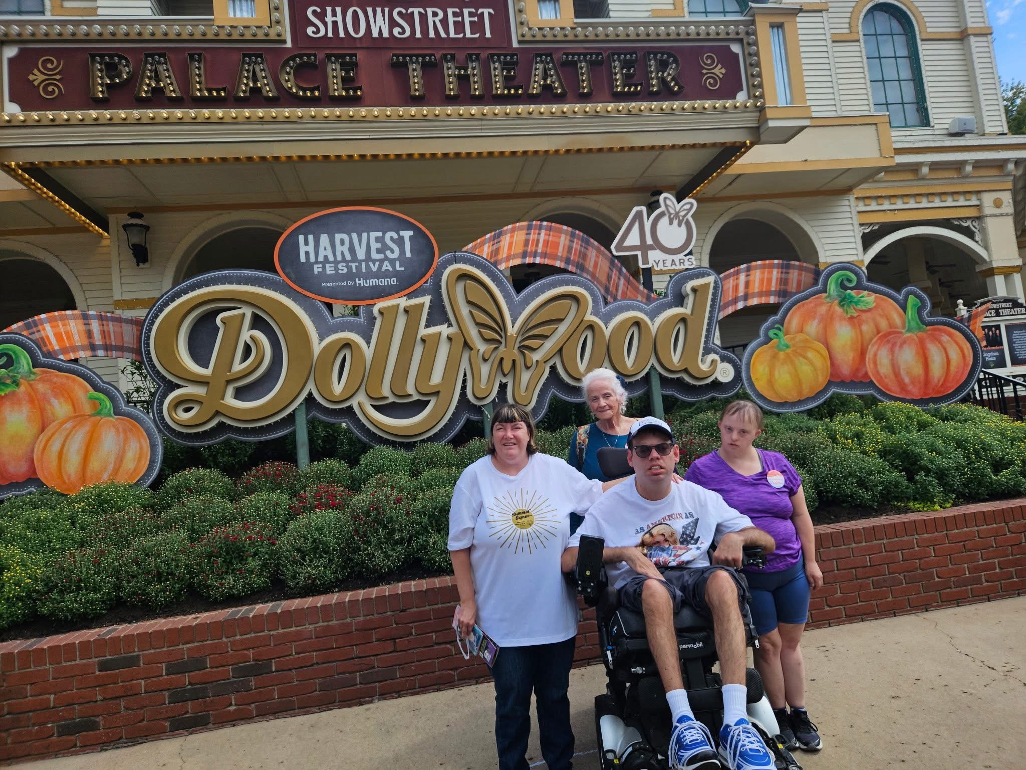A group of four people standing in front of the Dolly Parton-themed Harvest Festival sign at the Palace Theater, with pumpkins and autumn decorations around them.