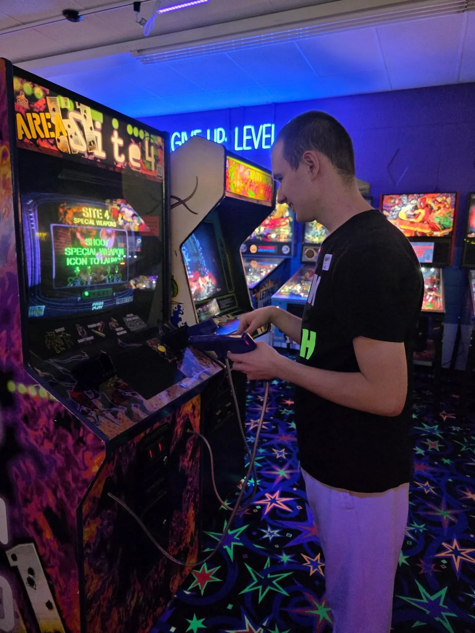 A man playing a vintage pinball machine at an arcade with neon and colorful lighting.