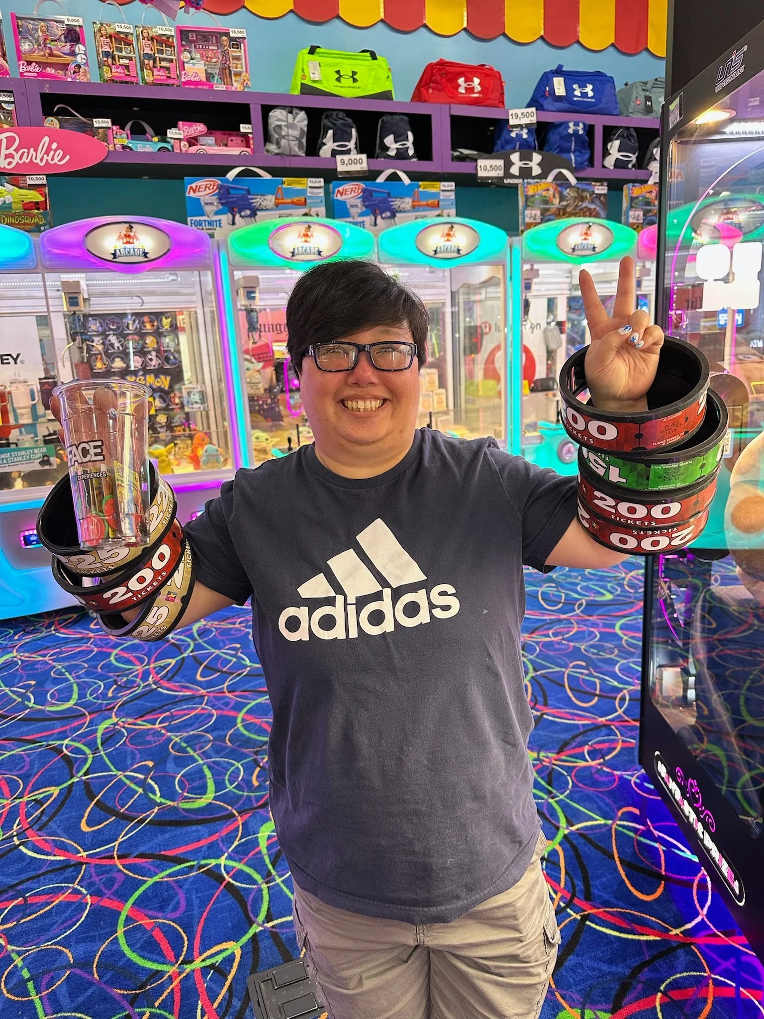 Person smiling and holding several arcade tickets in a colorful arcade environment with various game machines and prize shelves in the background.