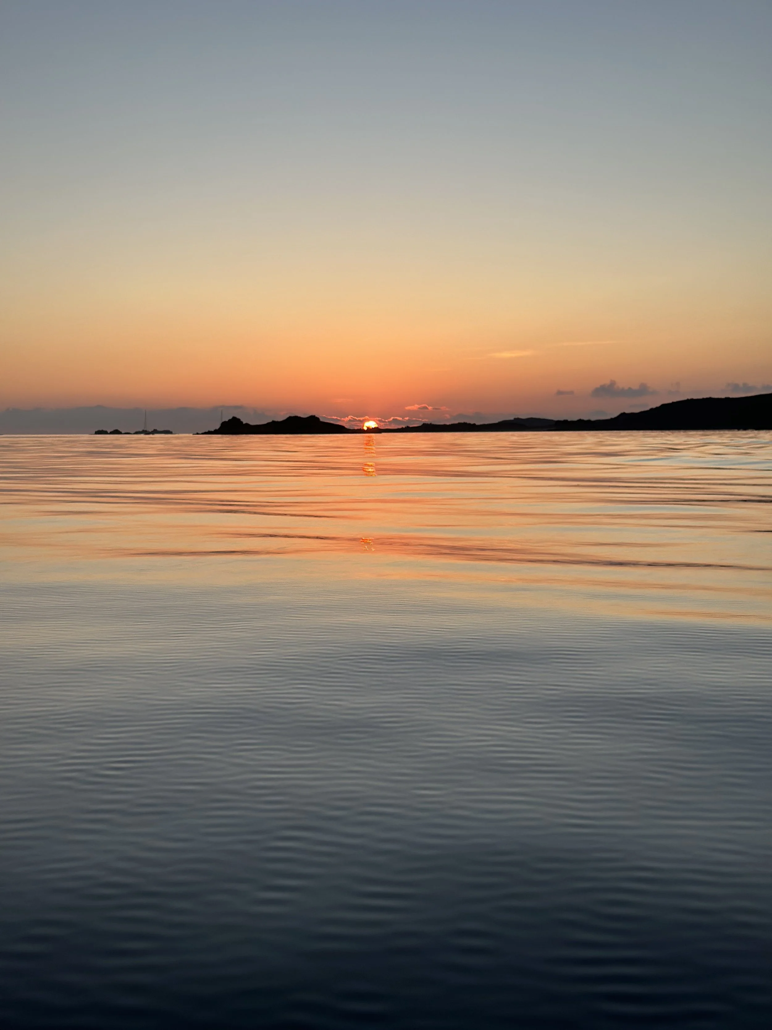 Orange sunset over the calm sea on St Mary's with small islands on the horizon.