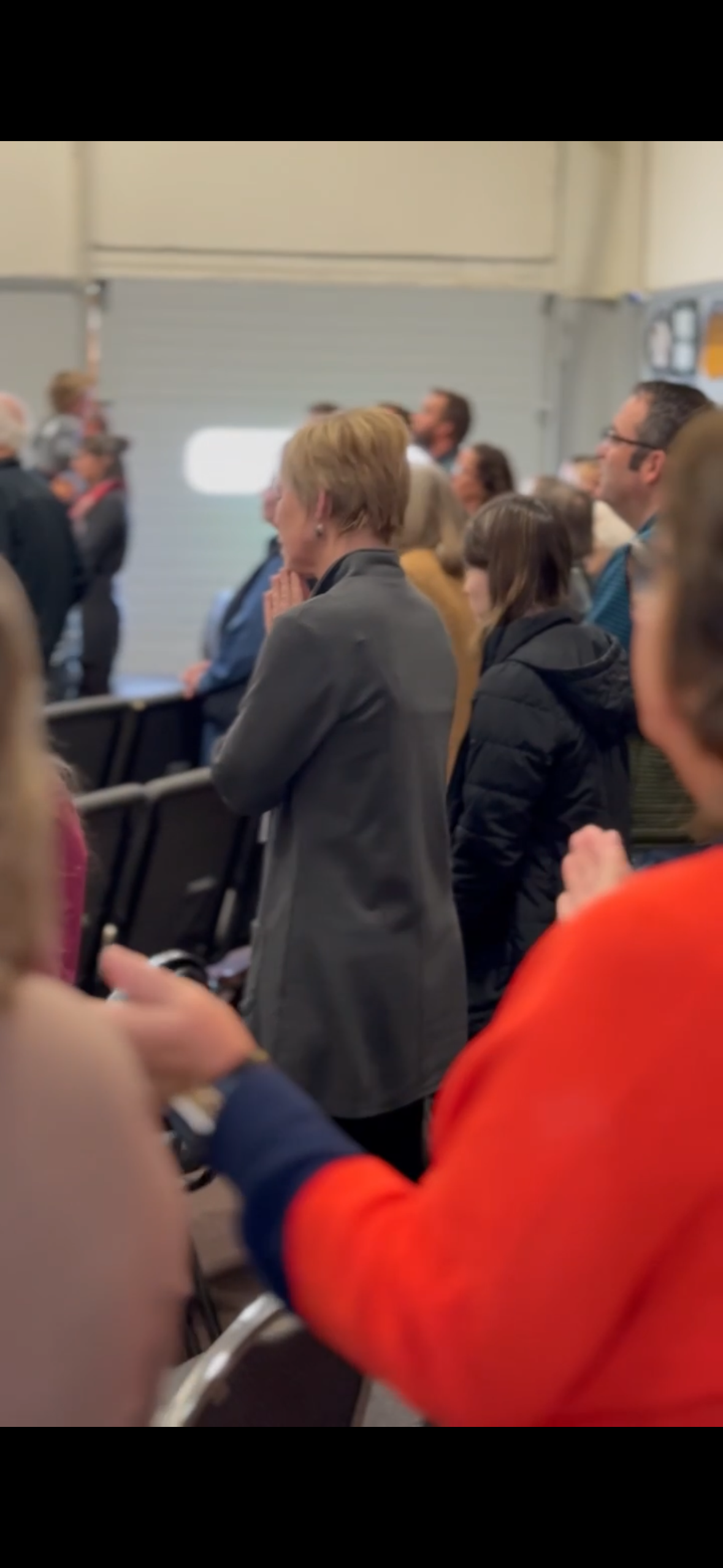 People standing and praying in an indoor space, possibly a church or community center.