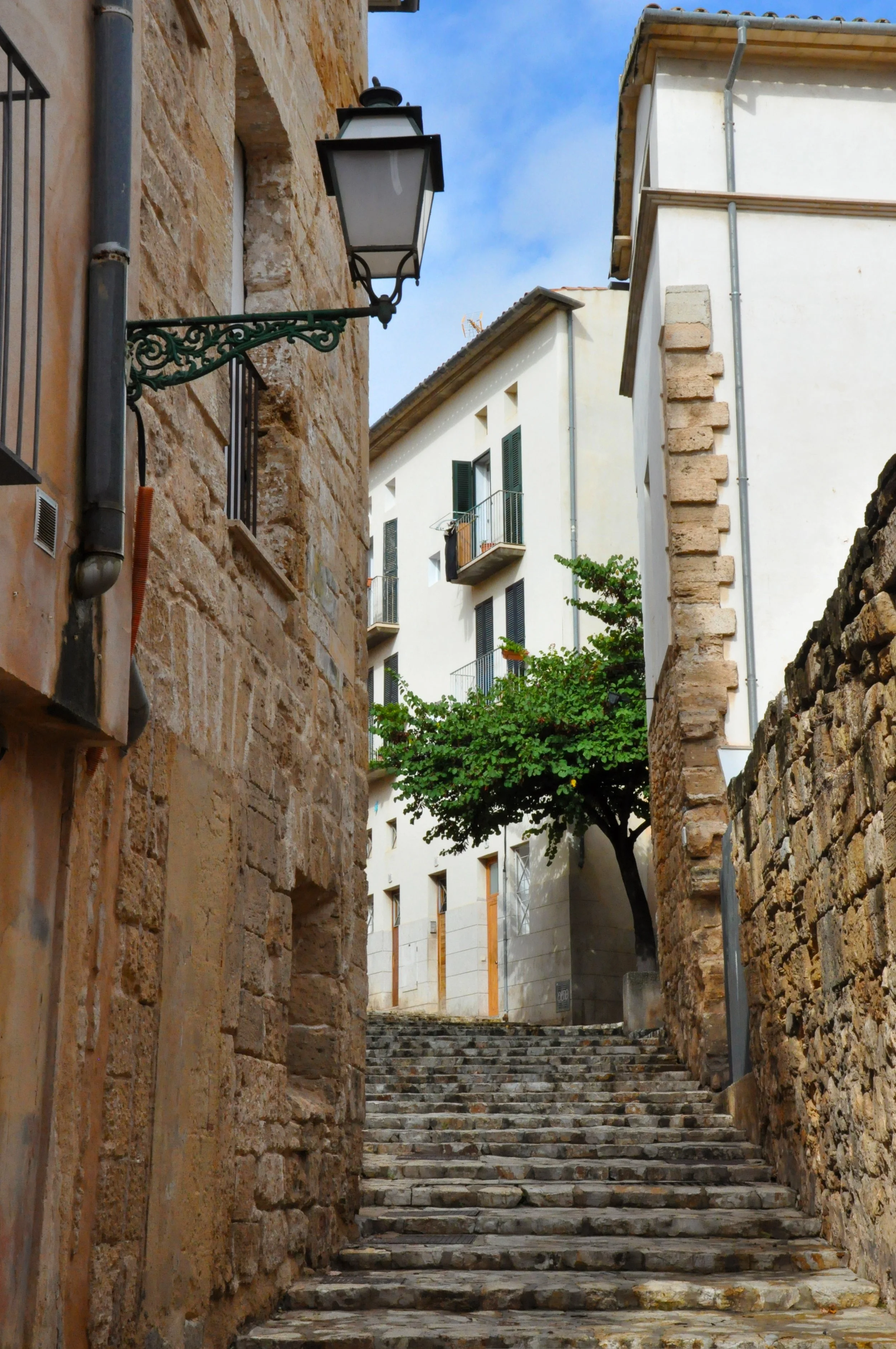 Calles empedradas con vieja arquitectura en un barrio europeo, con una lámpara de calle, árboles y casas blancas.