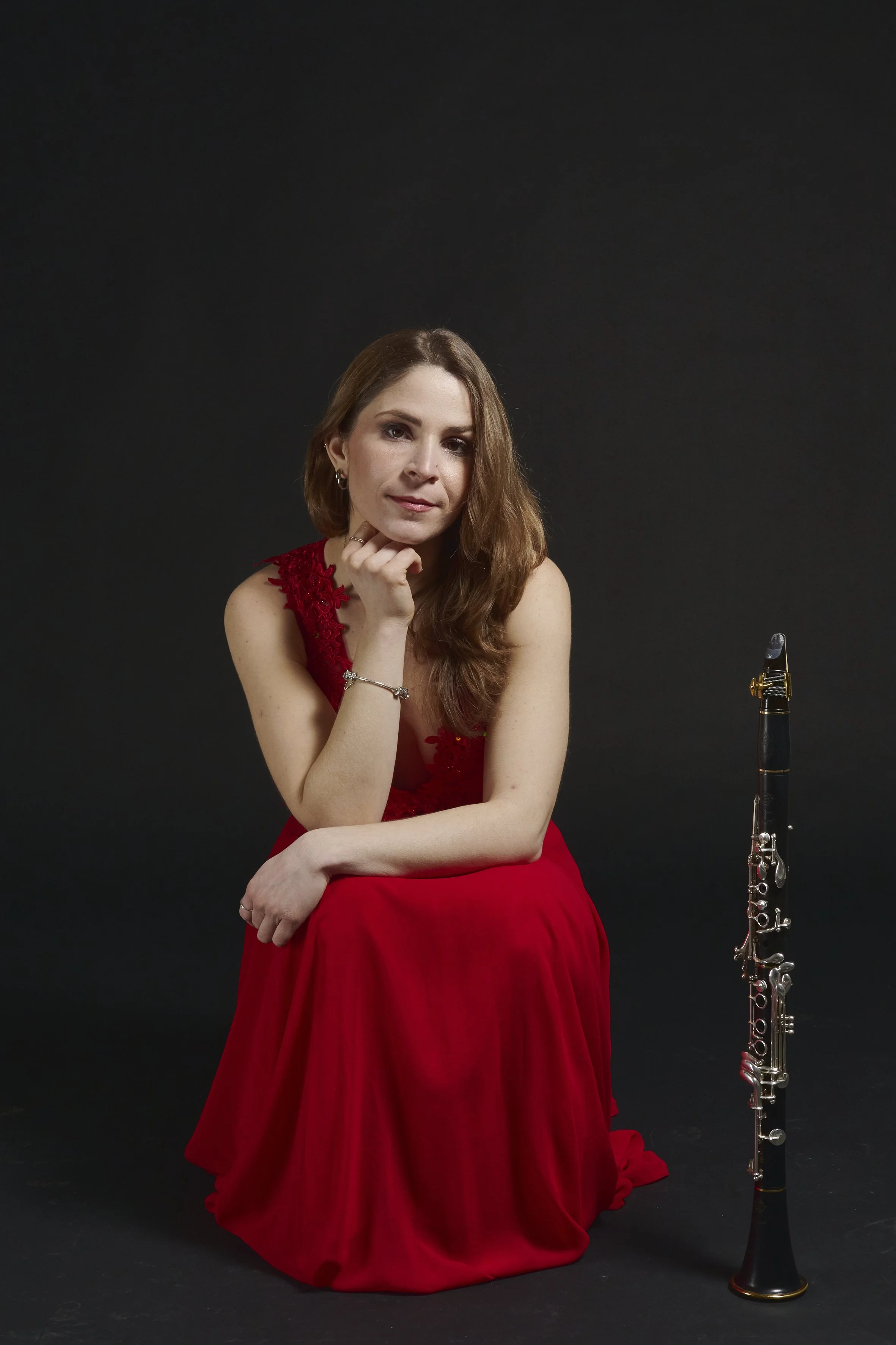 Maura Marinucci, Retrato de una mujer con vestido rojo, sentada con un clarinete al lado, fondo negro.