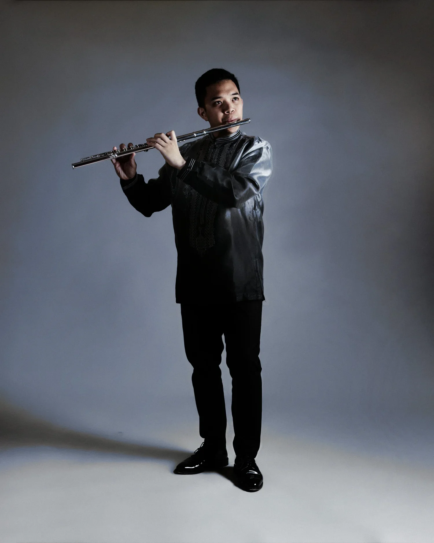 Rafael adobas, Joven tocando la flauta en un estudio con fondo gris oscuro.