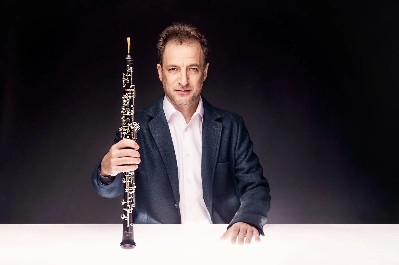 Dudu Carmel, Hombre con barba en traje sosteniendo un clarinete en un fondo oscuro.