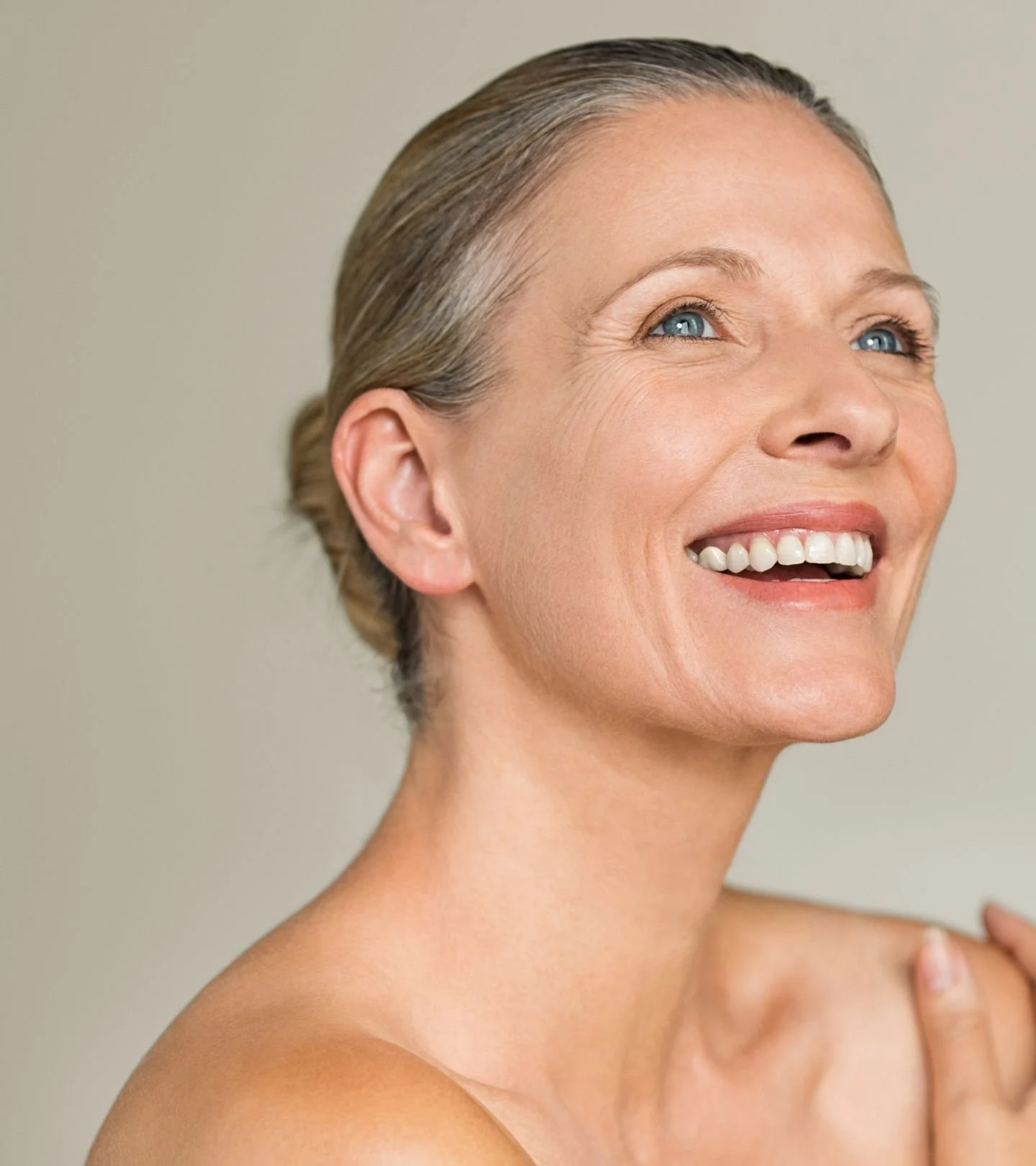A smiling woman with short, gray hair and blue eyes, looking upward, with a light, neutral background.