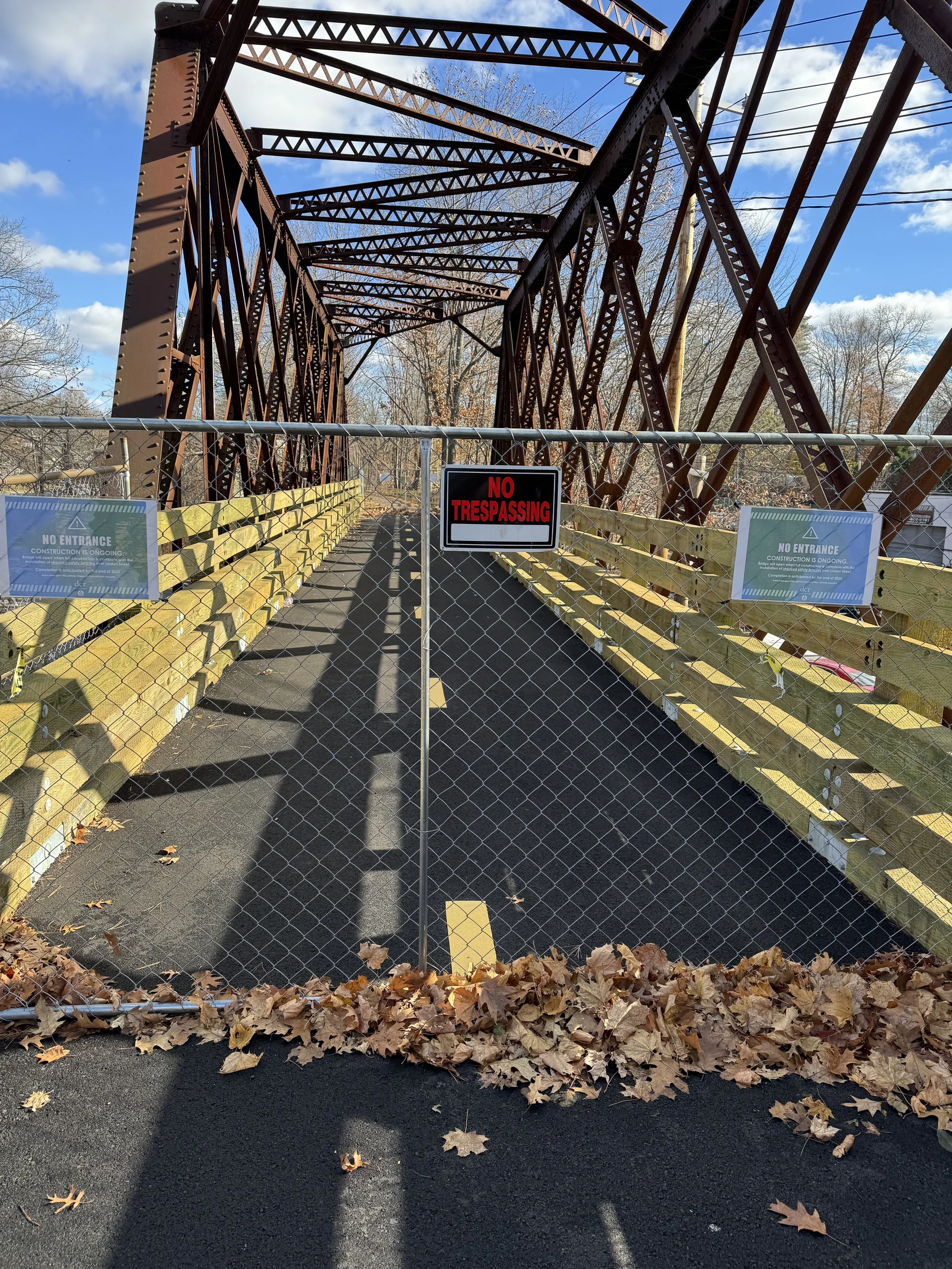 A fully constructed pedestrian bridge blocked by a fence with no trespassing and on-going construction signs