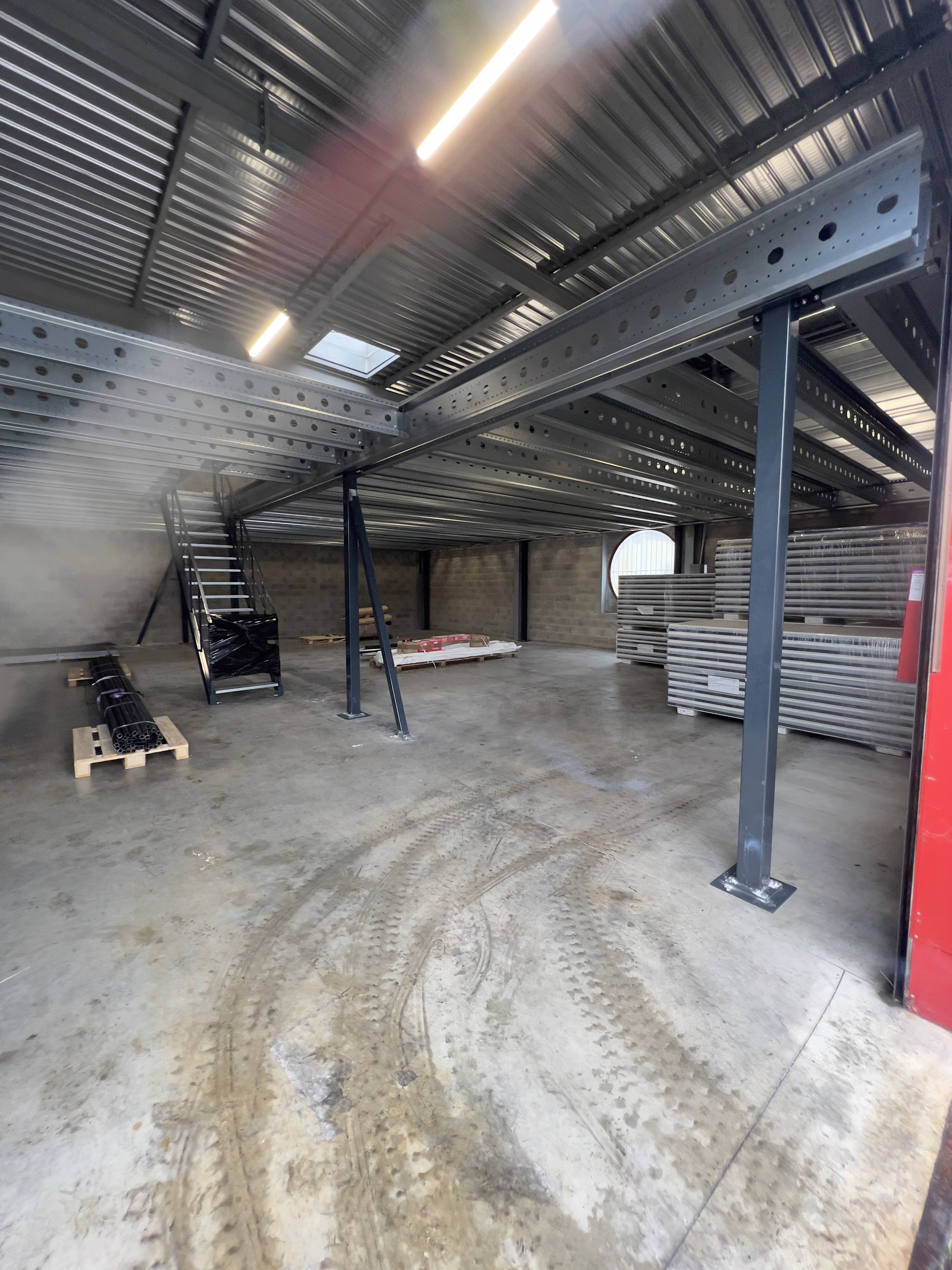 Interior of an industrial building under construction with metal framework, concrete floor, and some construction materials stored inside.