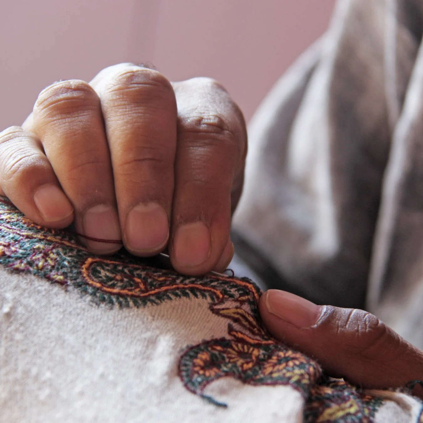 A close-up of a person's hand gently holding a colorful embroidered fabric.