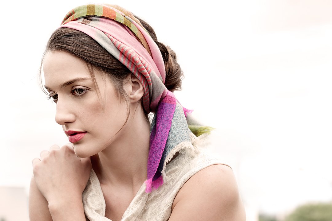 A woman with a colorful pashmina cashmere headscarf looking downward with a pensive expression.