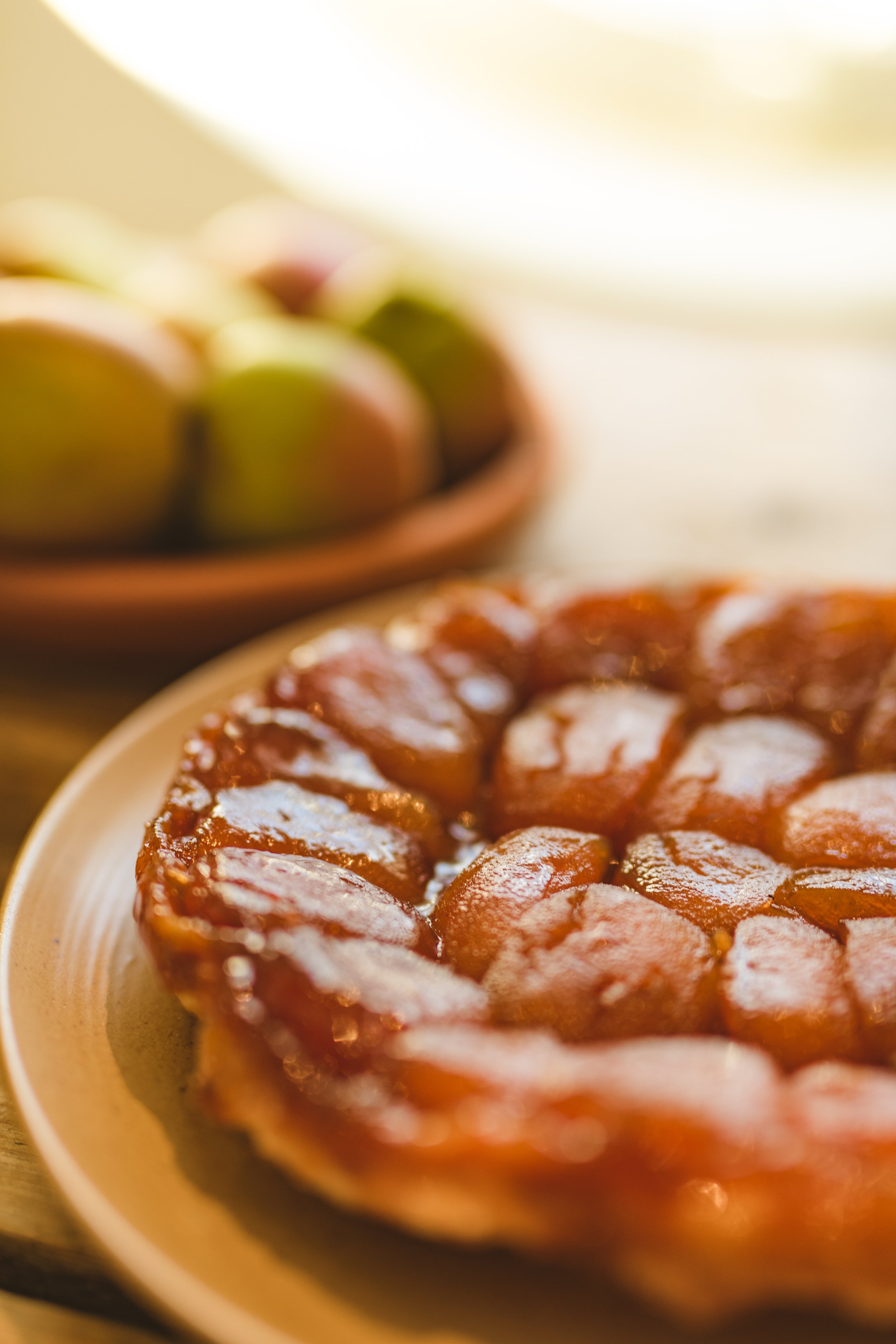Close-up of a plate of sliced cooked apples arranged in a circular pattern, with a bowl of whole apples in the background.