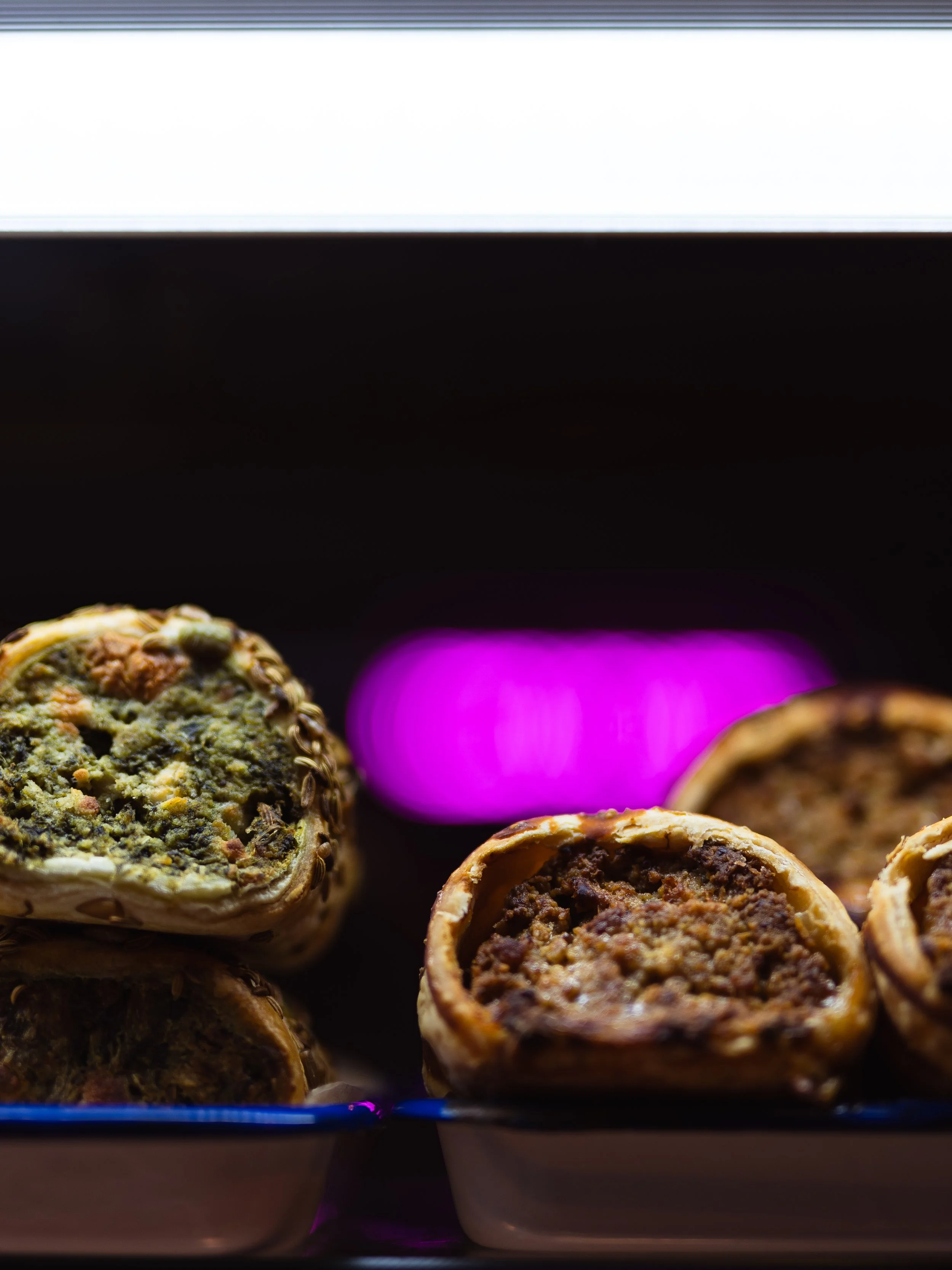 Close-up of cooked savory pastries with filling, in a baking dish, under a pink and white light.
