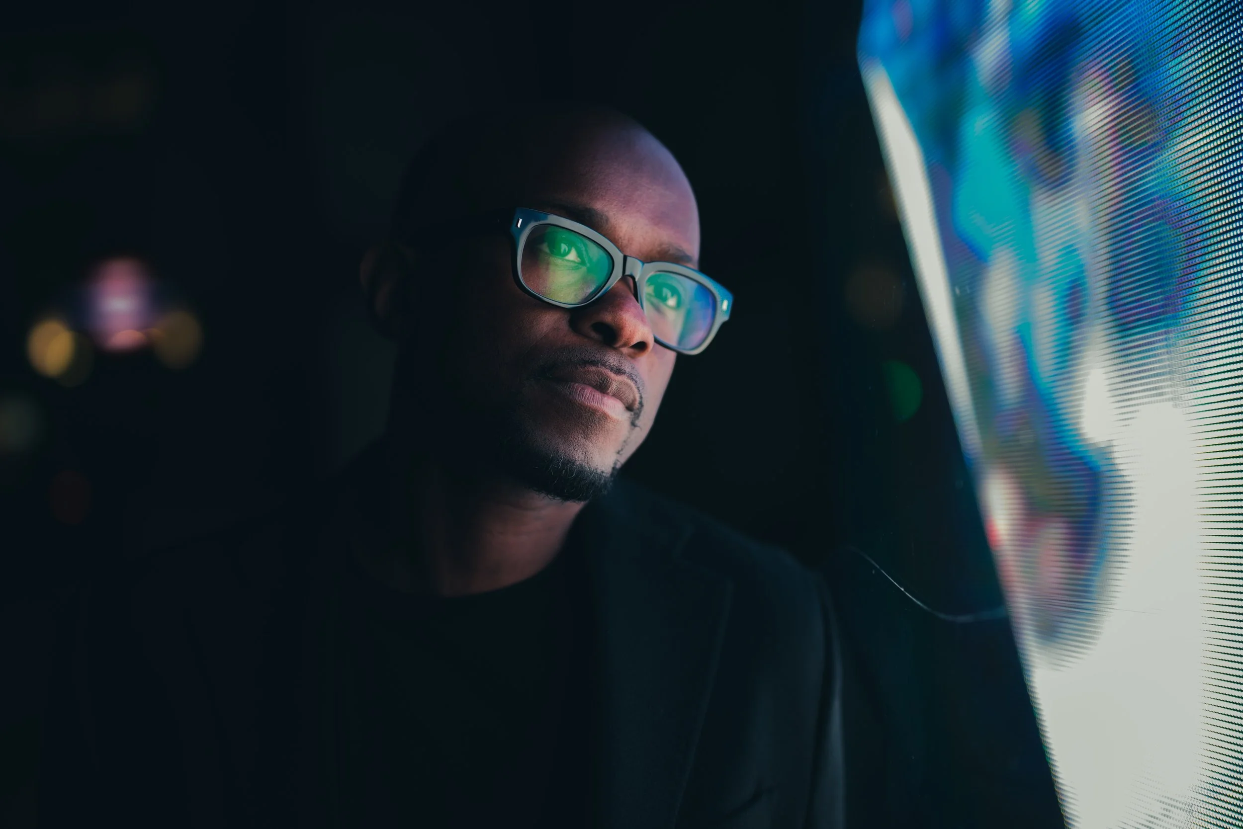 A man with glasses looking at a large screen with colorful data visualizations in a dark room.