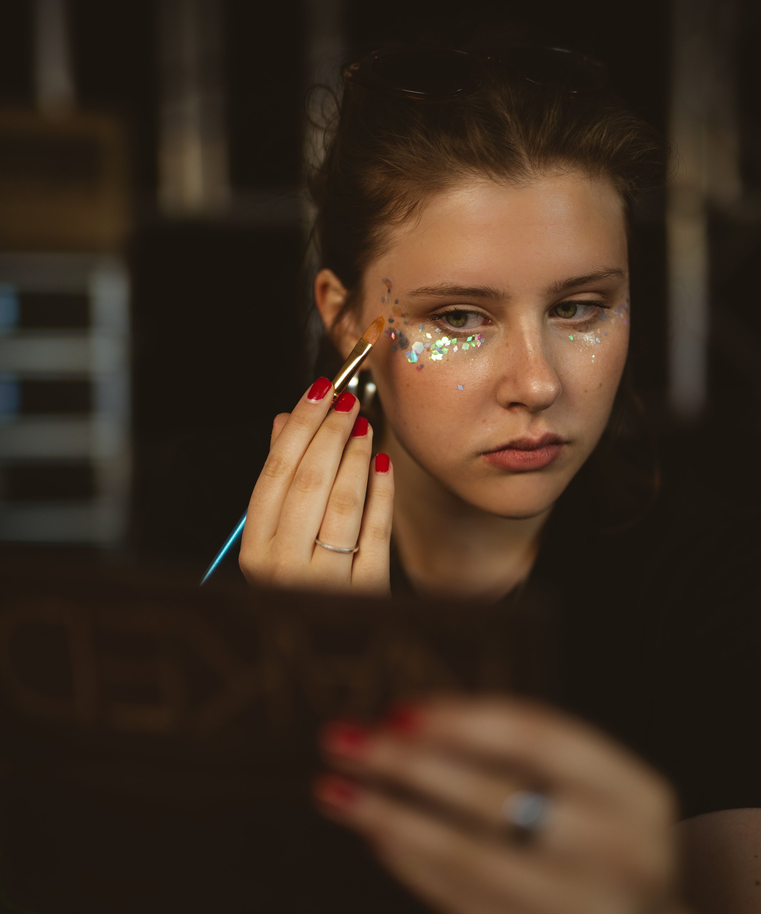 A woman with makeup applying glitter around her eyes using a small brush.