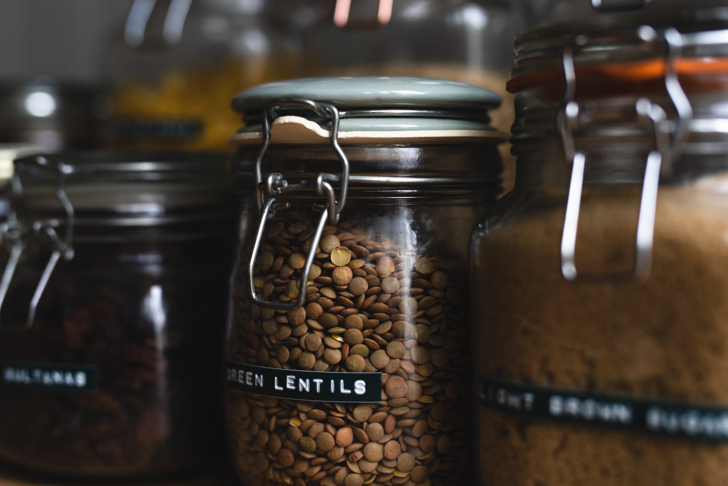 Glass jars with metal clasps containing lentils and spices on a shelf.