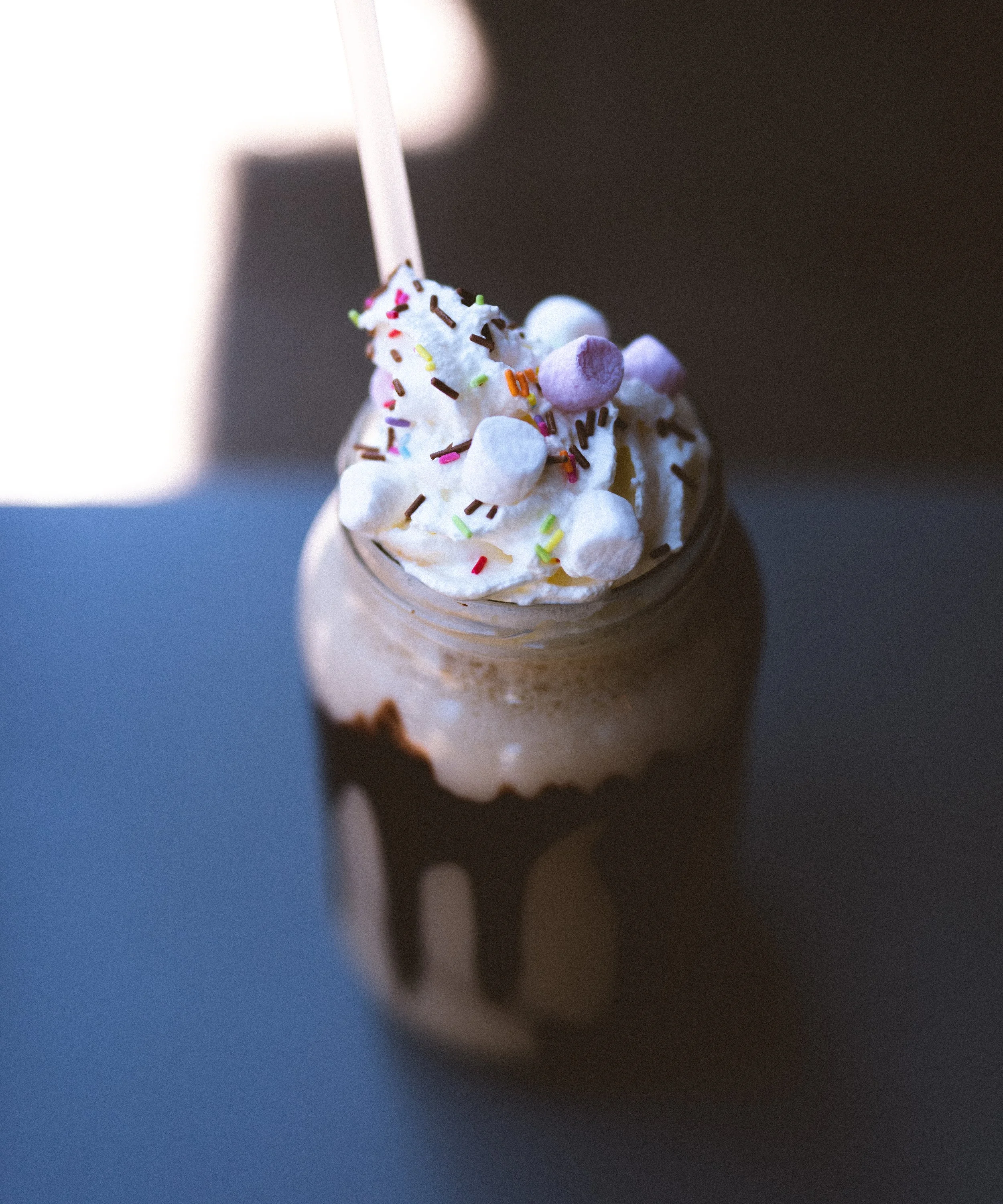 Chocolate milkshake topped with whipped cream, colorful sprinkles, mini marshmallows, and a straw.