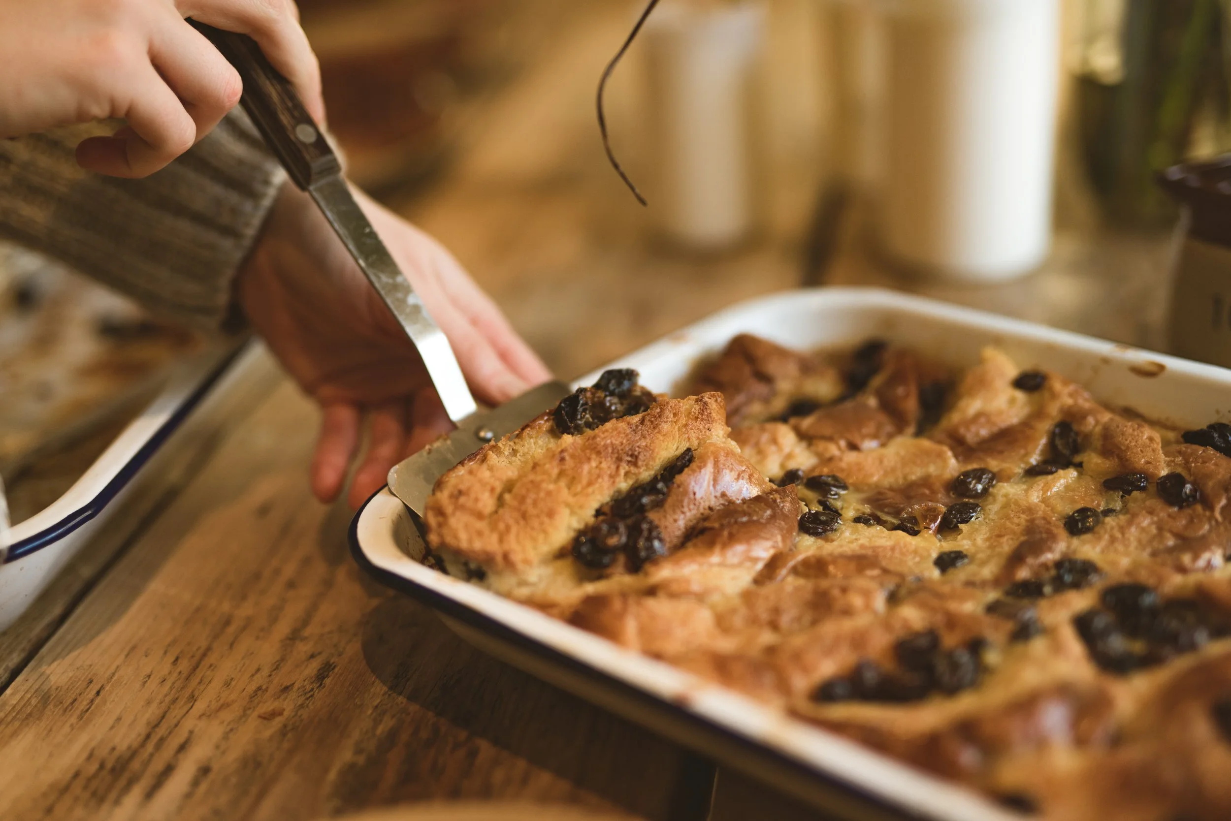 Person serving freshly baked apple crisp with raisins from a baking dish onto a plate.
