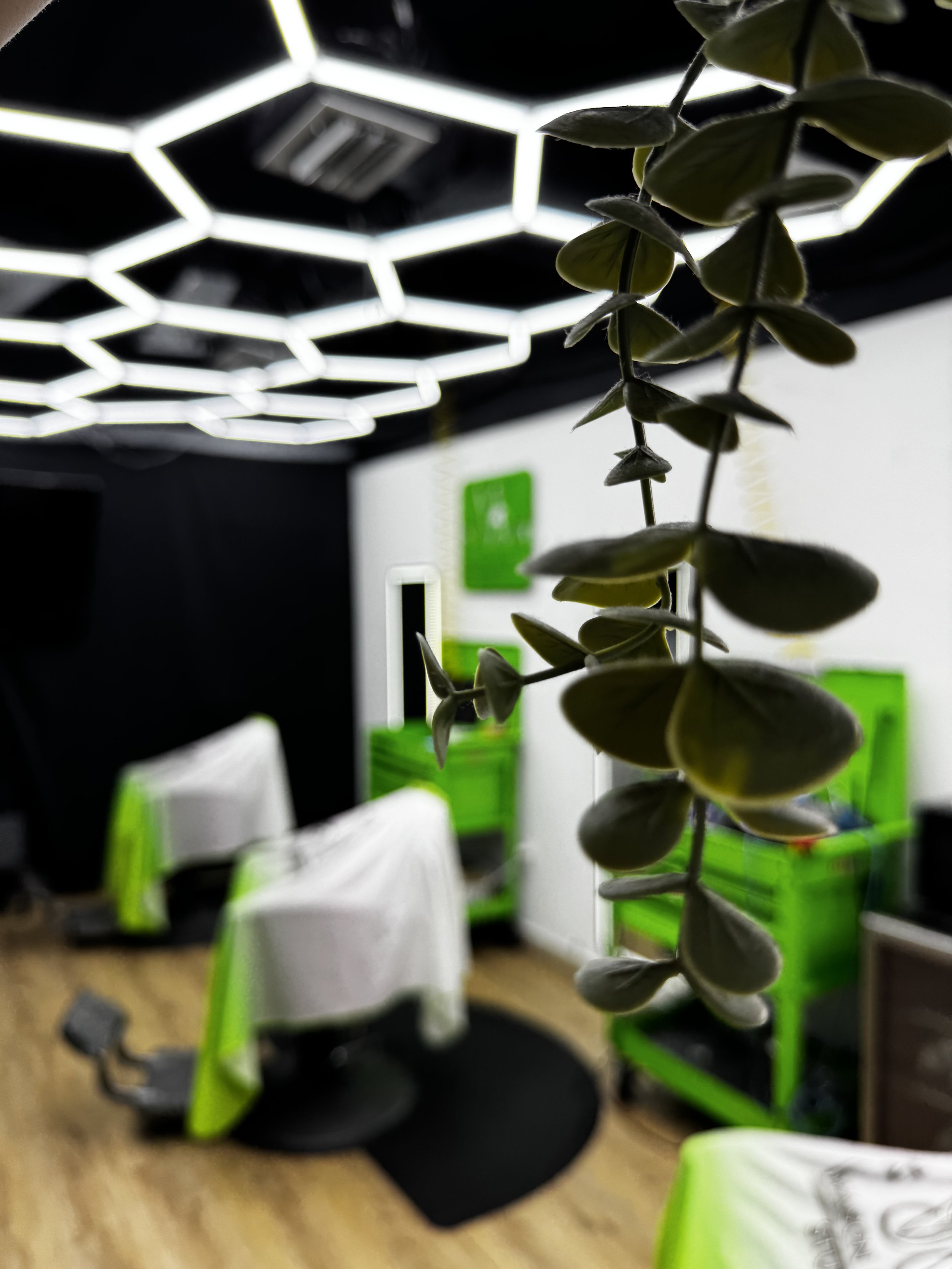 Interior de una oficina moderna con sillas blancas y verdes, mesas con manteles blancos, paredes blancas y negras, y un techo con luces de forma hexagonal.