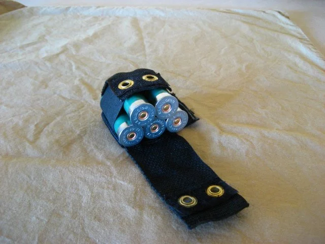 A black fabric holder containing six AA batteries, placed on a light-colored fabric surface.